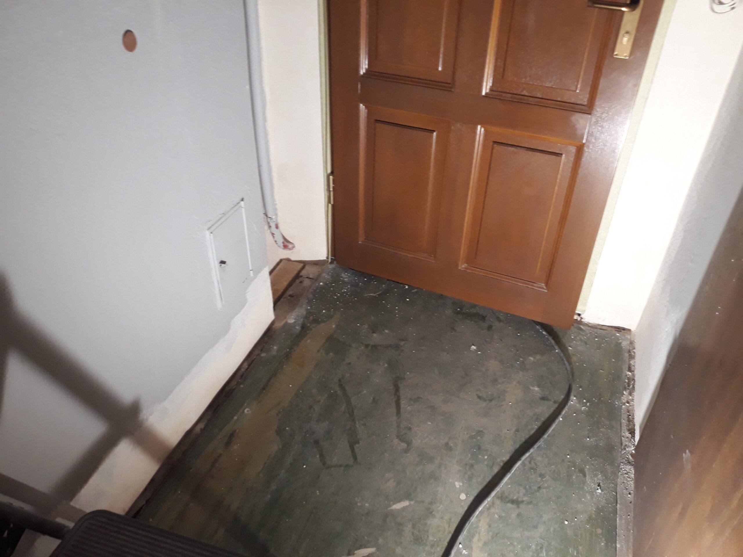 Surowe podłoże przy drzwiach wejściowych z widoczną instalacją elektryczną, przygotowane do dalszych prac wykończeniowych i montażowych.