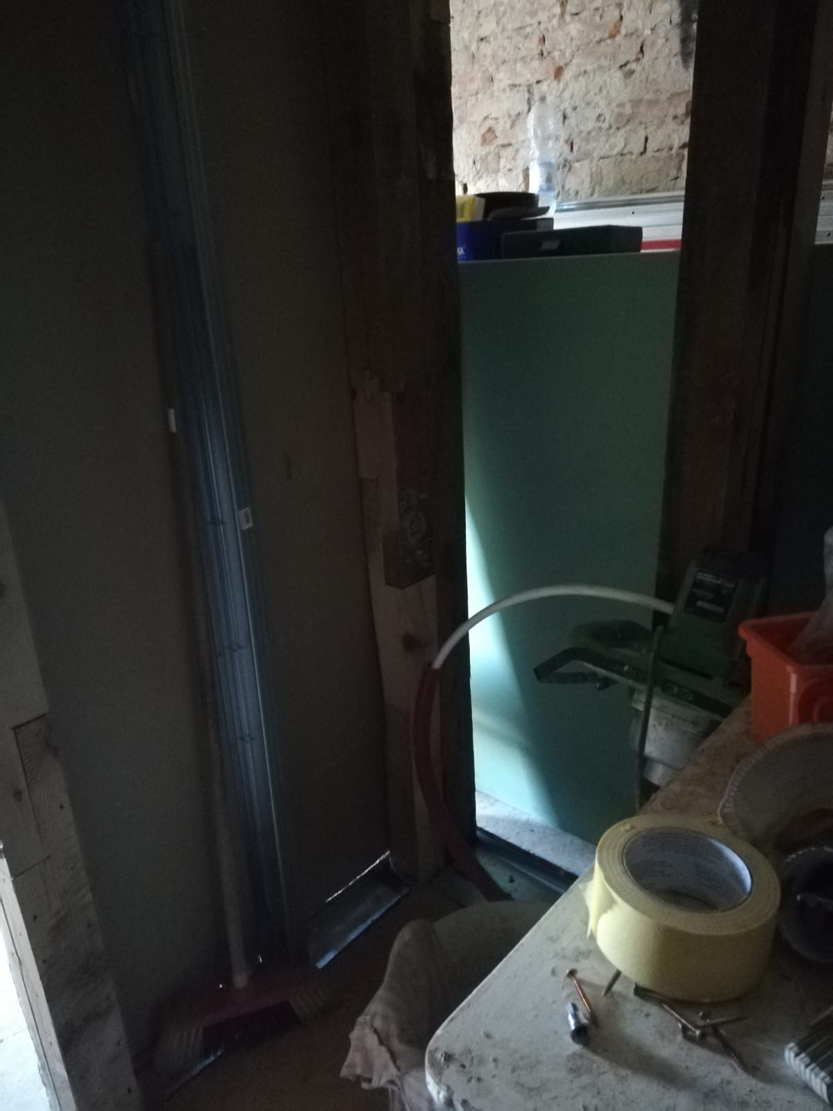 Otwór drzwiowy w trakcie remontu z widoczną konstrukcją, płytą gipsową i narzędziami na blacie roboczym