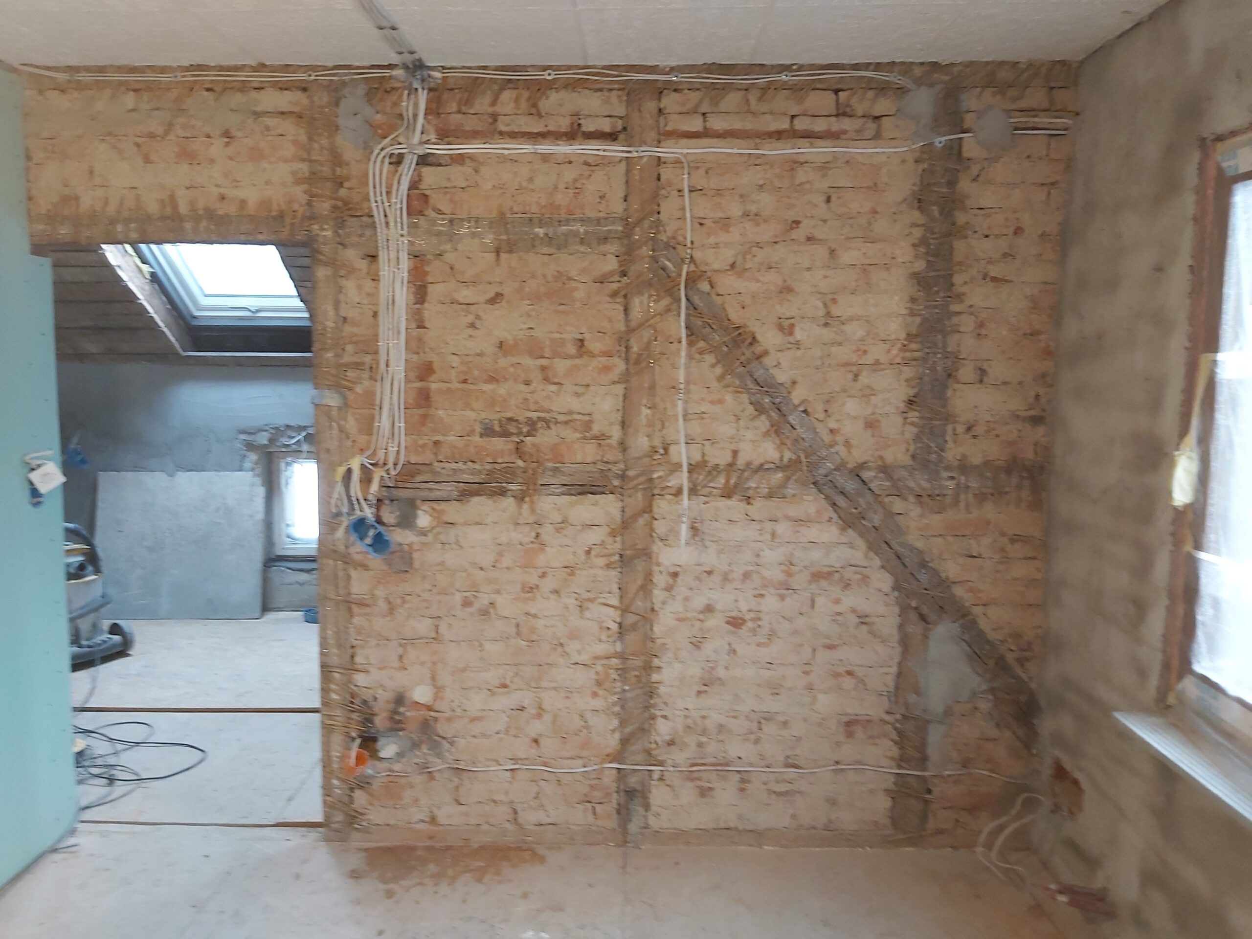 Odsłonięta ceglana ściana z rozprowadzoną instalacją elektryczną, przygotowana do dalszych prac wykończeniowych.