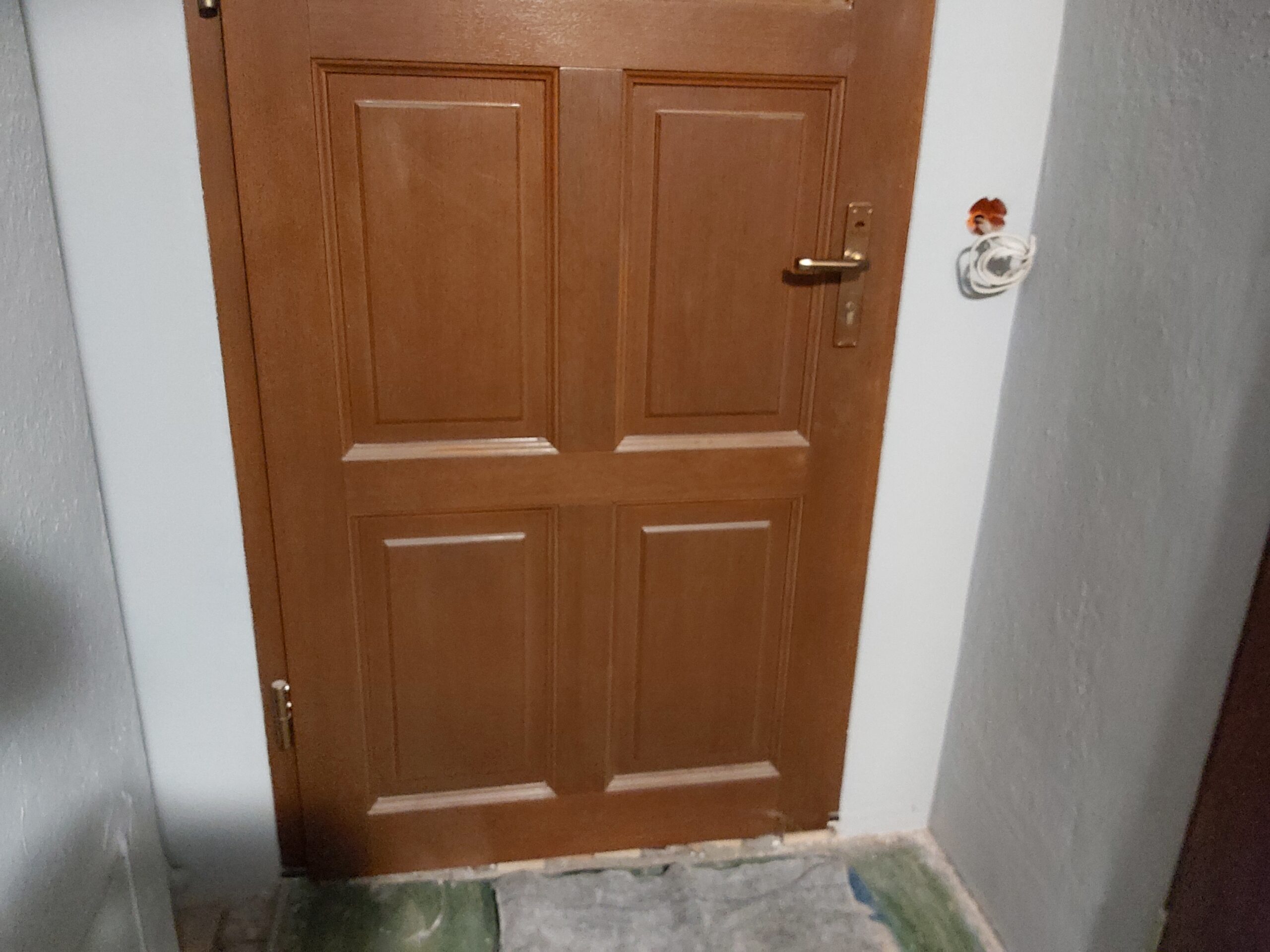 Brązowe drzwi wewnętrzne z płycinami, zamontowane w białej ościeży podczas prac remontowych, z nieukończoną posadzką przy progu.