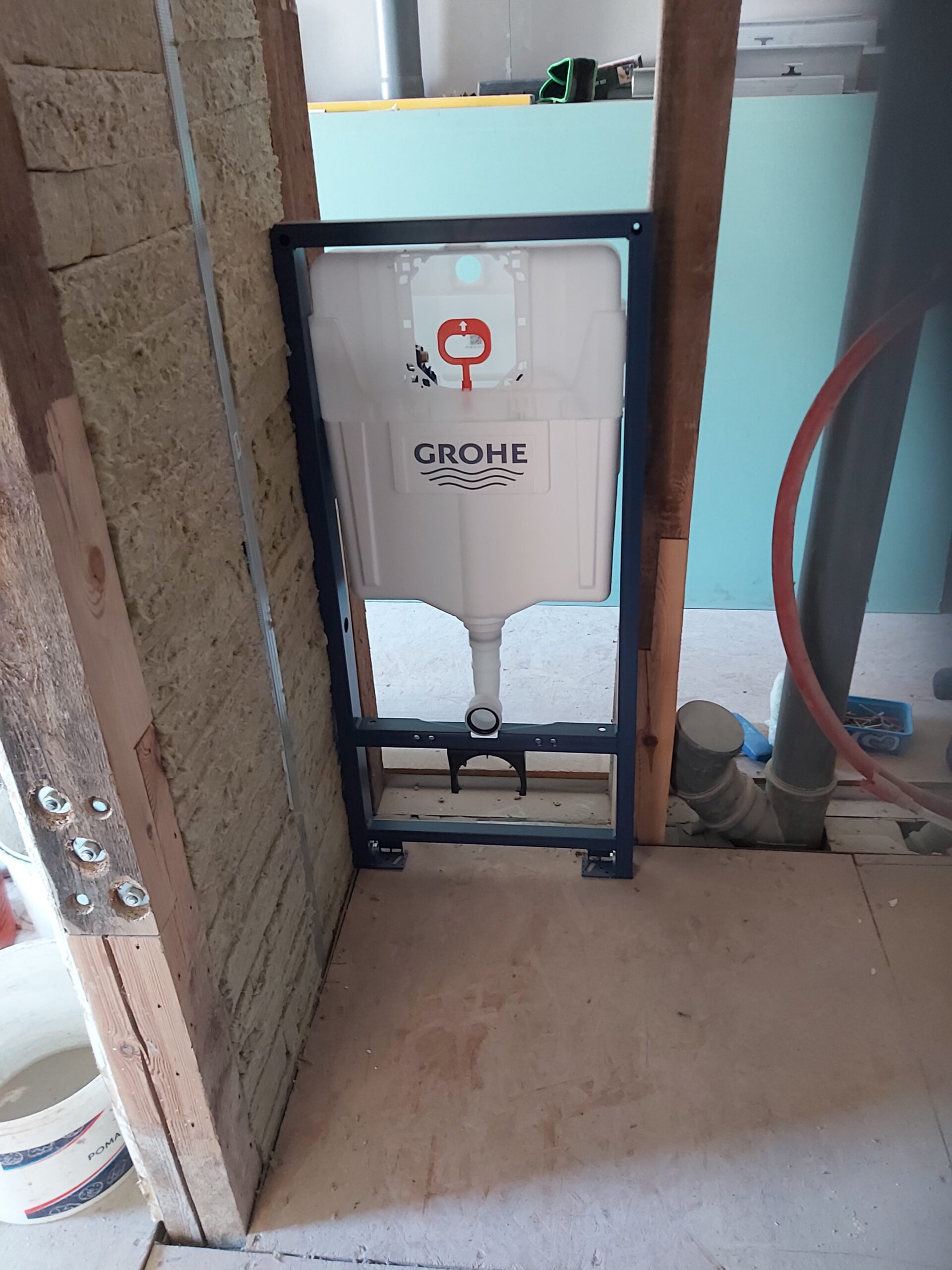 Stelaż podtynkowy WC marki Grohe zamontowany w konstrukcji ściany, widoczny zbiornik spłukujący, elementy mocujące oraz instalacje sanitarne podczas prac wykończeniowych.