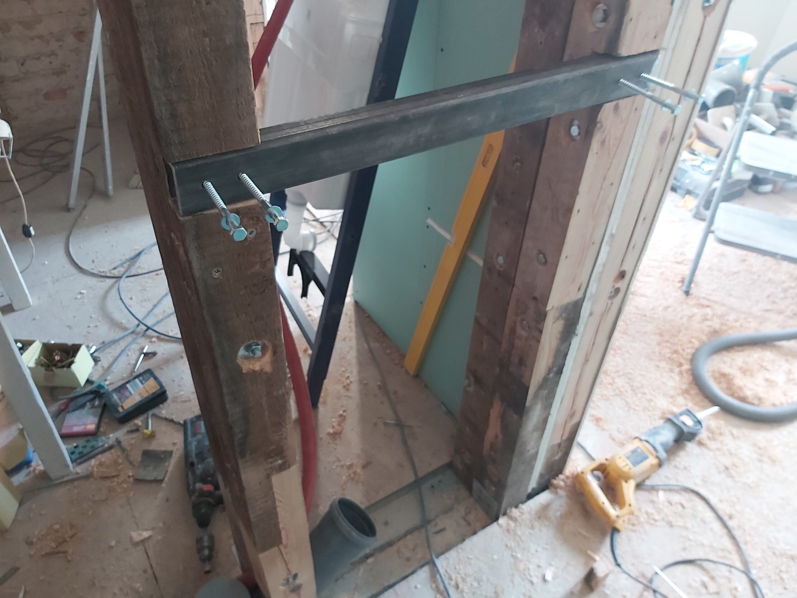 Metalowy profil wzmacniający zamontowany w drewnianej konstrukcji ściany działowej pod stelaż WC, z widocznymi śrubami regulacyjnymi i instalacją w trakcie prac montażowych.