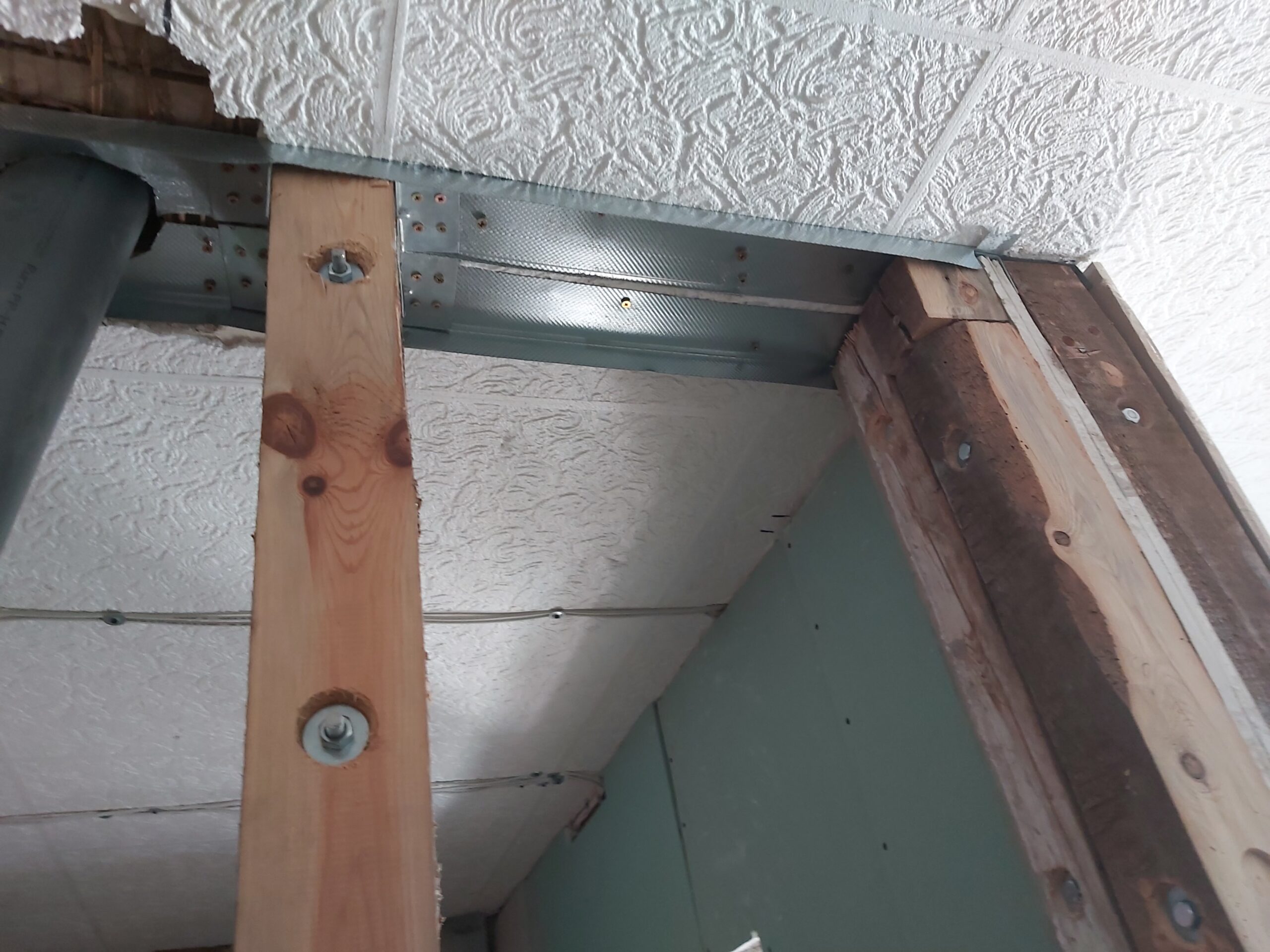 Połączenie drewnianych słupków z metalowym profilem przy suficie w konstrukcji ściany