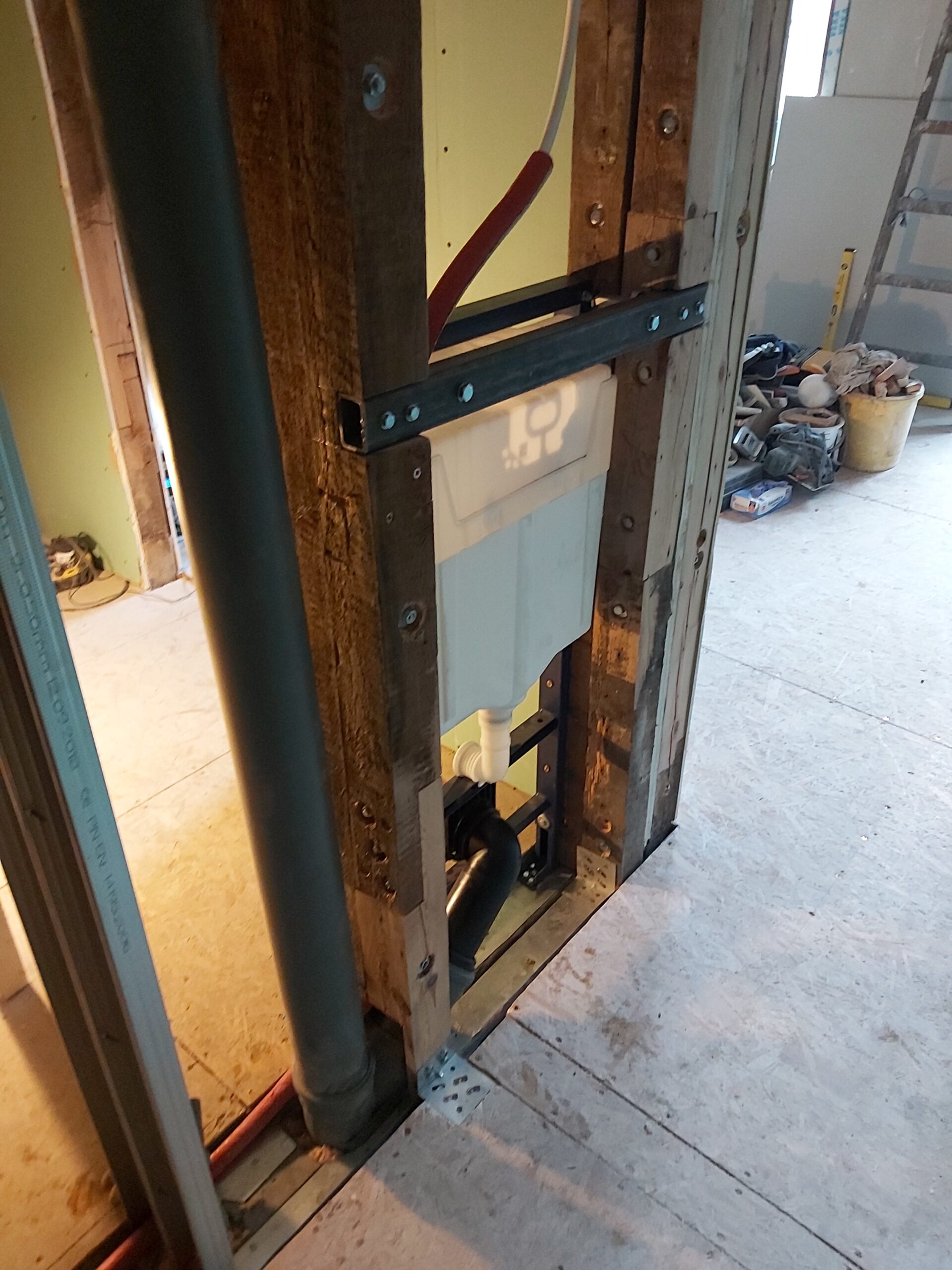 Widok stelaża WC zamontowanego w konstrukcji drewniano-metalowej, z widocznym odpływem kanalizacyjnym i instalacją przed zamknięciem ściany płytami g-k.