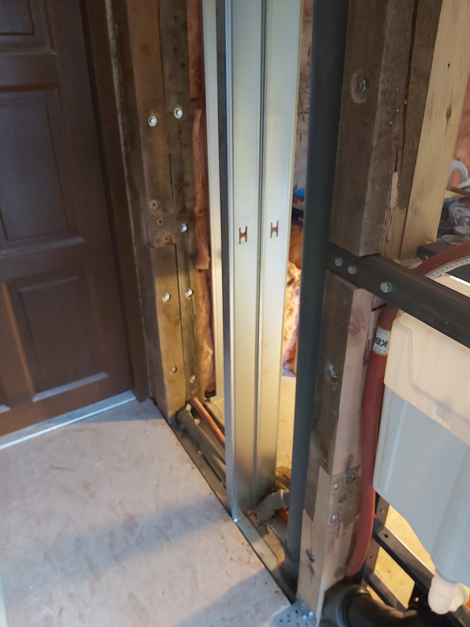 Fragment konstrukcji ściany z profilami metalowymi i drewnianymi belkami przy podtynkowym stelażu WC, z widoczną instalacją hydrauliczną oraz przygotowaniem pod zabudowę płytami gipsowo-kartonowymi.