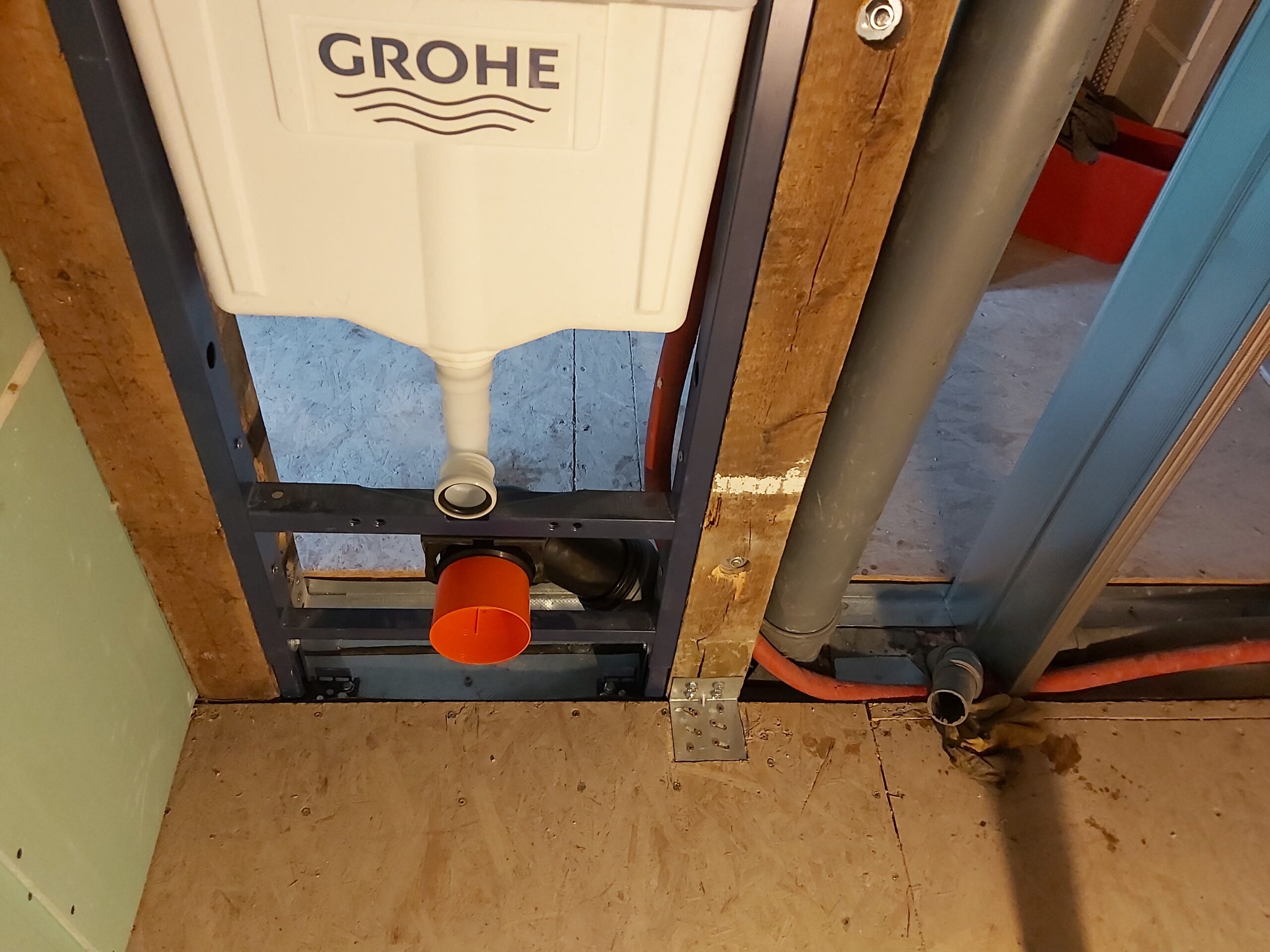 Dolna część podtynkowego stelaża WC Grohe z widocznym podłączeniem odpływu kanalizacyjnego, pionem kanalizacyjnym oraz instalacją hydrauliczną w trakcie prac remontowych.