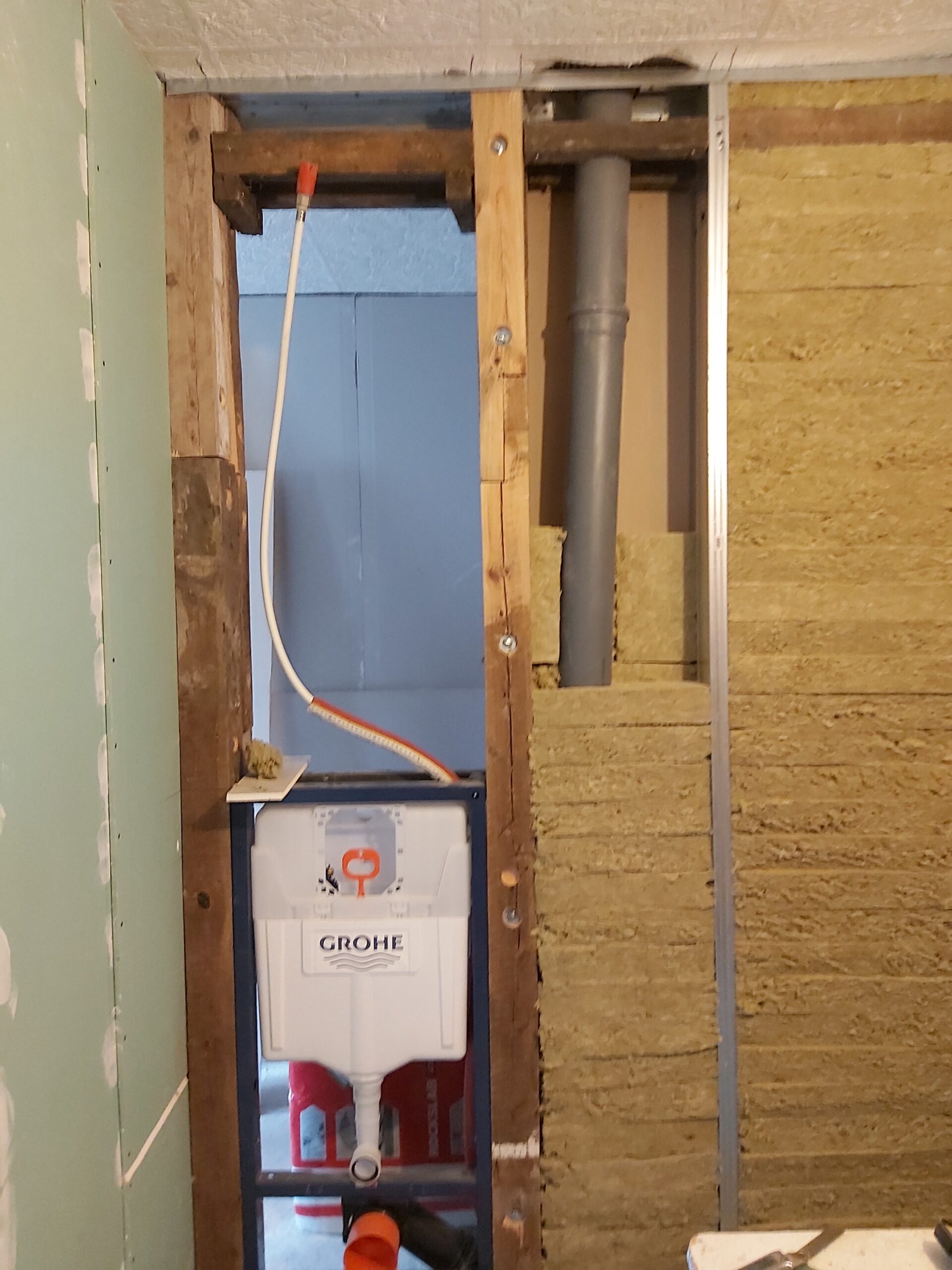 Podtynkowy stelaż WC marki Grohe zamontowany w ścianie szkieletowej, z widocznym pionem kanalizacyjnym, izolacją z wełny mineralnej oraz instalacją wodną i elektryczną w trakcie prac remontowych.