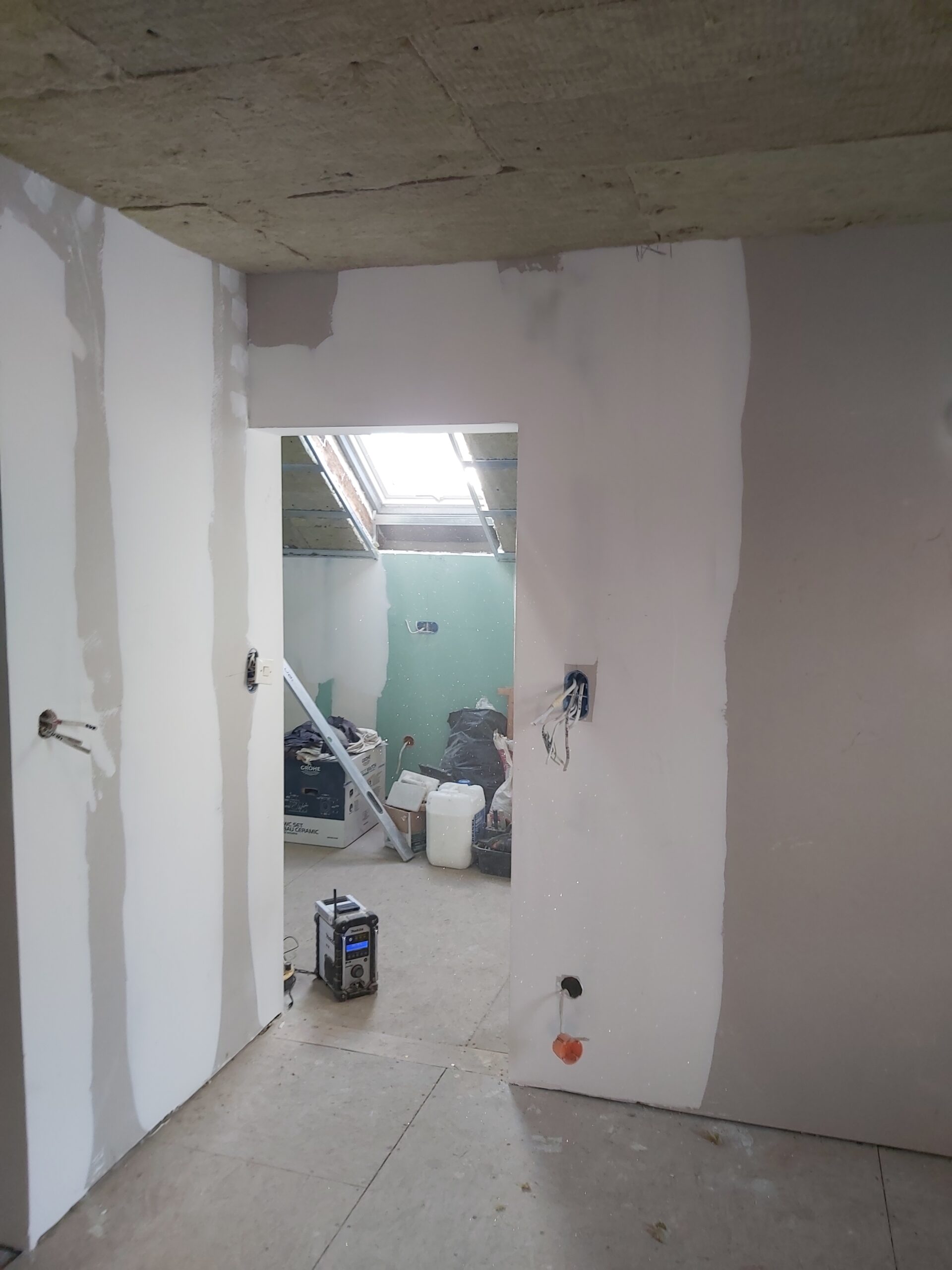 Ściana z płyt gipsowo-kartonowych w trakcie szpachlowania, z widocznymi pasami masy, otworem drzwiowym bez ościeżnicy oraz instalacją elektryczną przygotowaną pod montaż osprzętu.