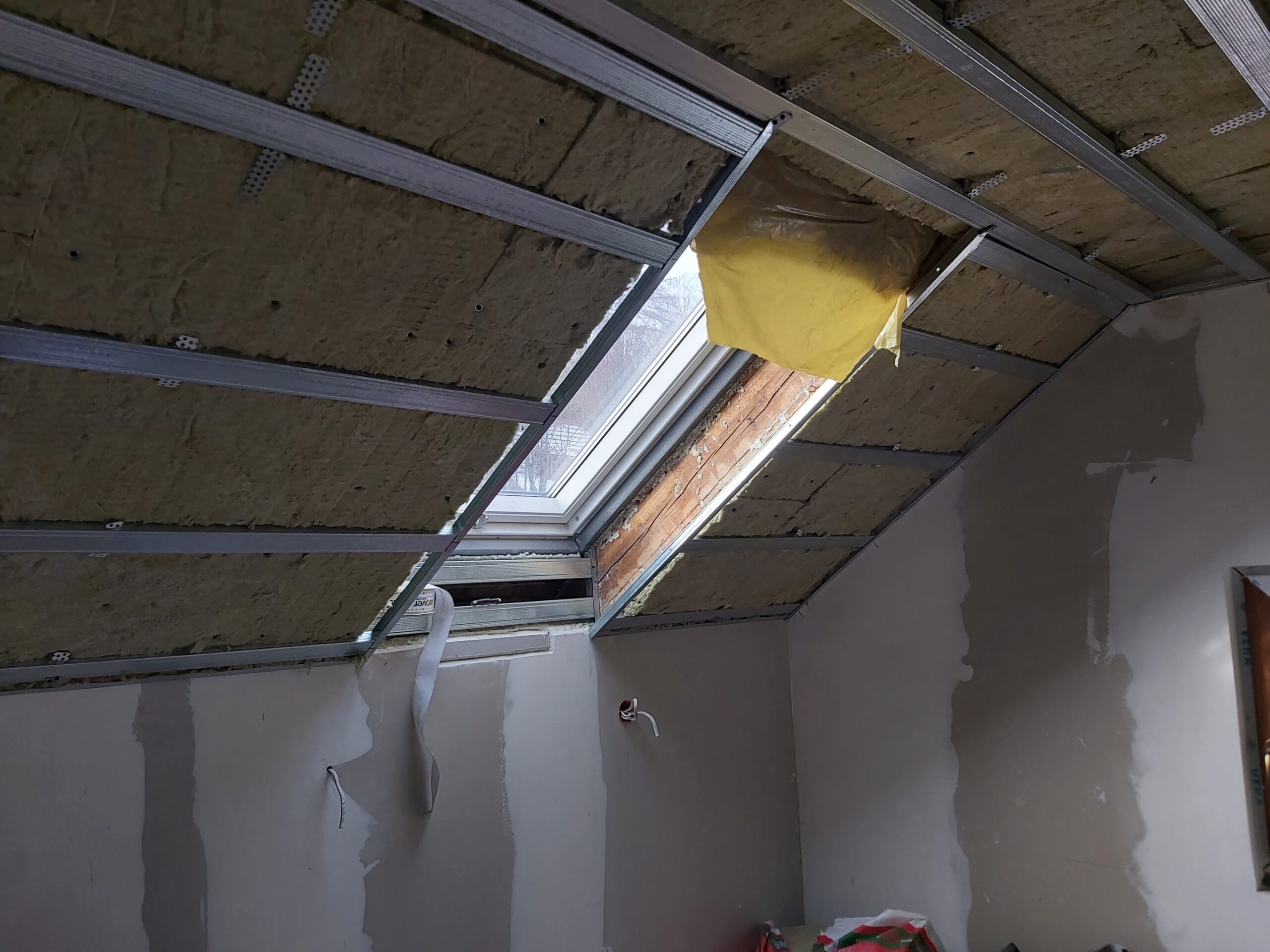 Okno dachowe w trakcie montażu sufitu poddasza z izolacją i profilami stalowymi