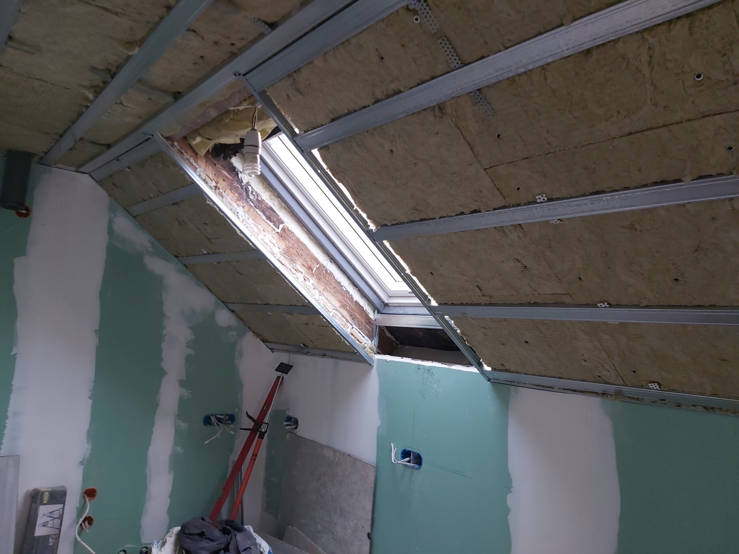 Okno dachowe podczas prac wykończeniowych na poddaszu, widoczna konstrukcja stalowa i izolacja