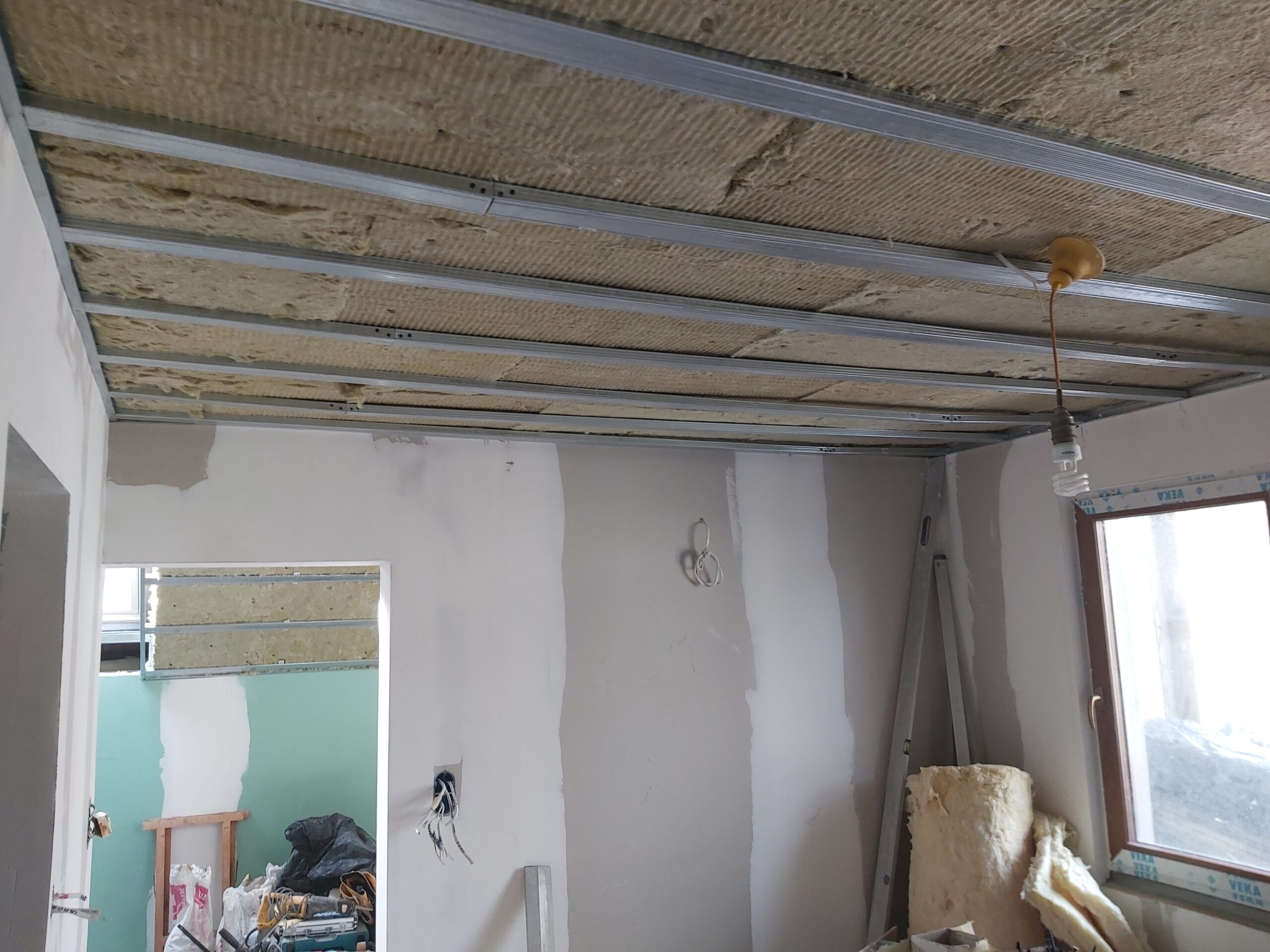 Pomieszczenie w trakcie remontu z odsłoniętą konstrukcją sufitu, izolacją oraz przygotowanymi ścianami pod dalsze prace