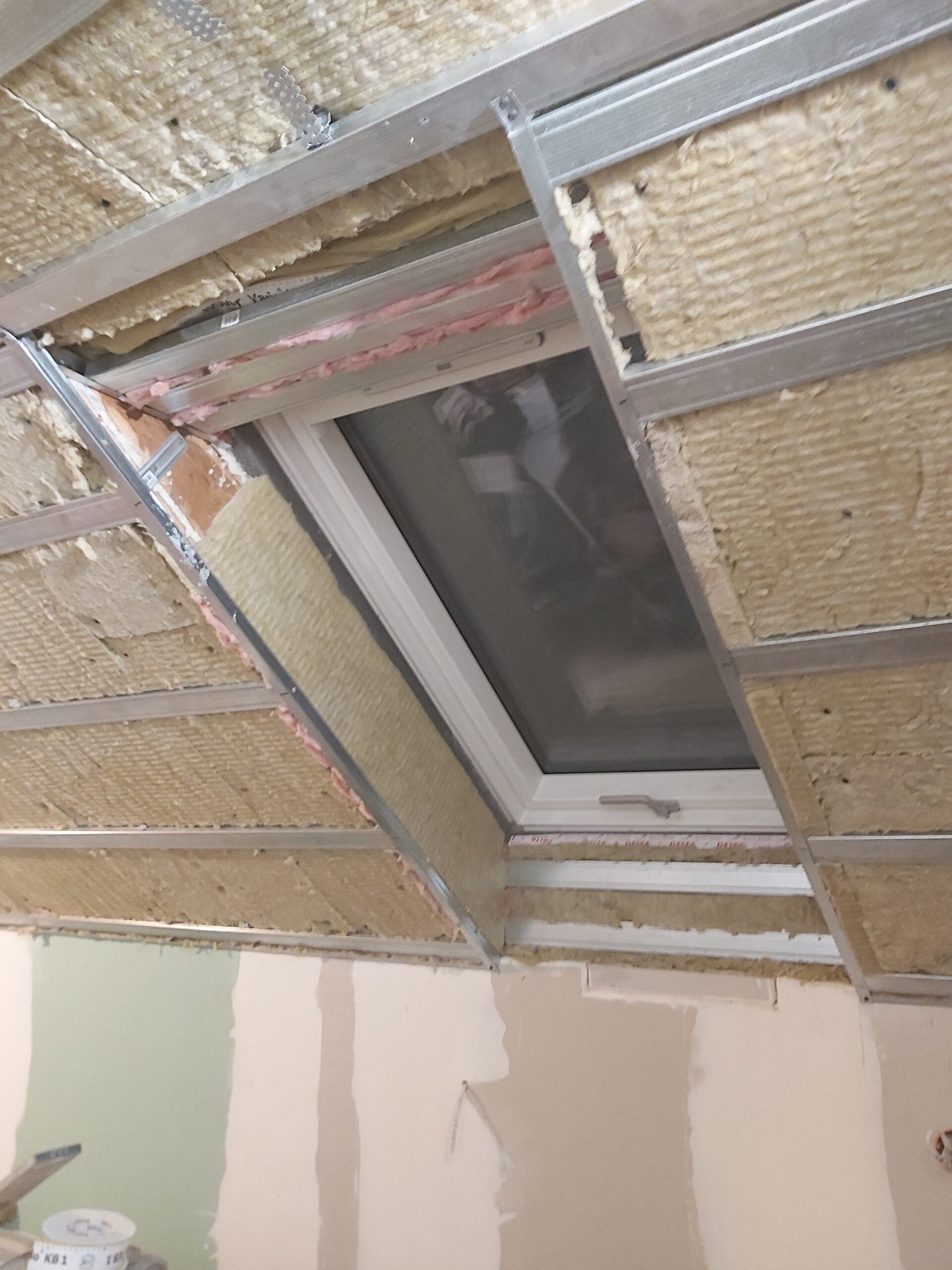 Konstrukcja sufitu poddasza z oknem dachowym, widoczna izolacja i profile metalowe