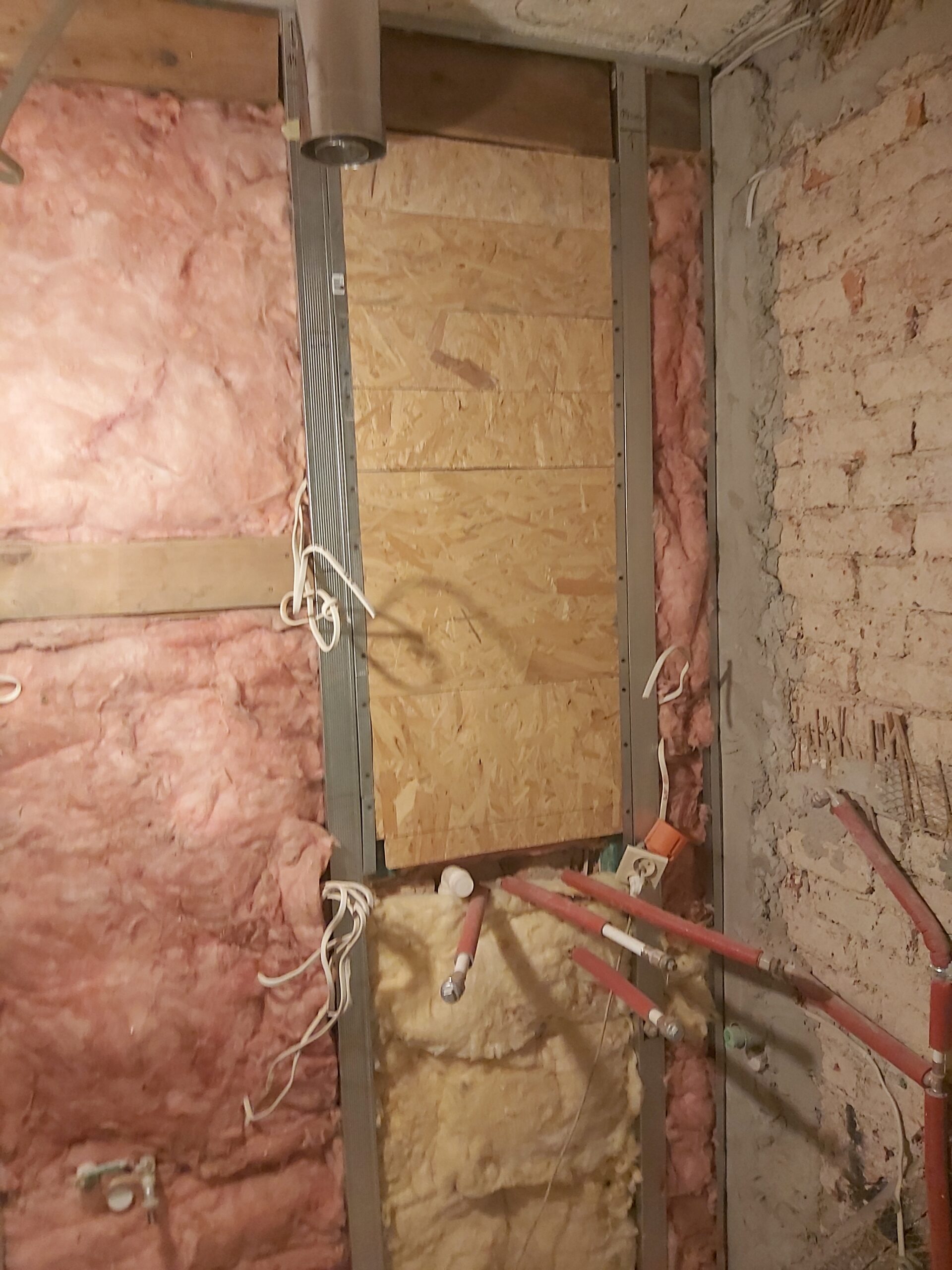 Ocieplona ściana w trakcie remontu z widoczną wełną izolacyjną, metalowym stelażem oraz fragmentami instalacji hydraulicznej i elektrycznej.