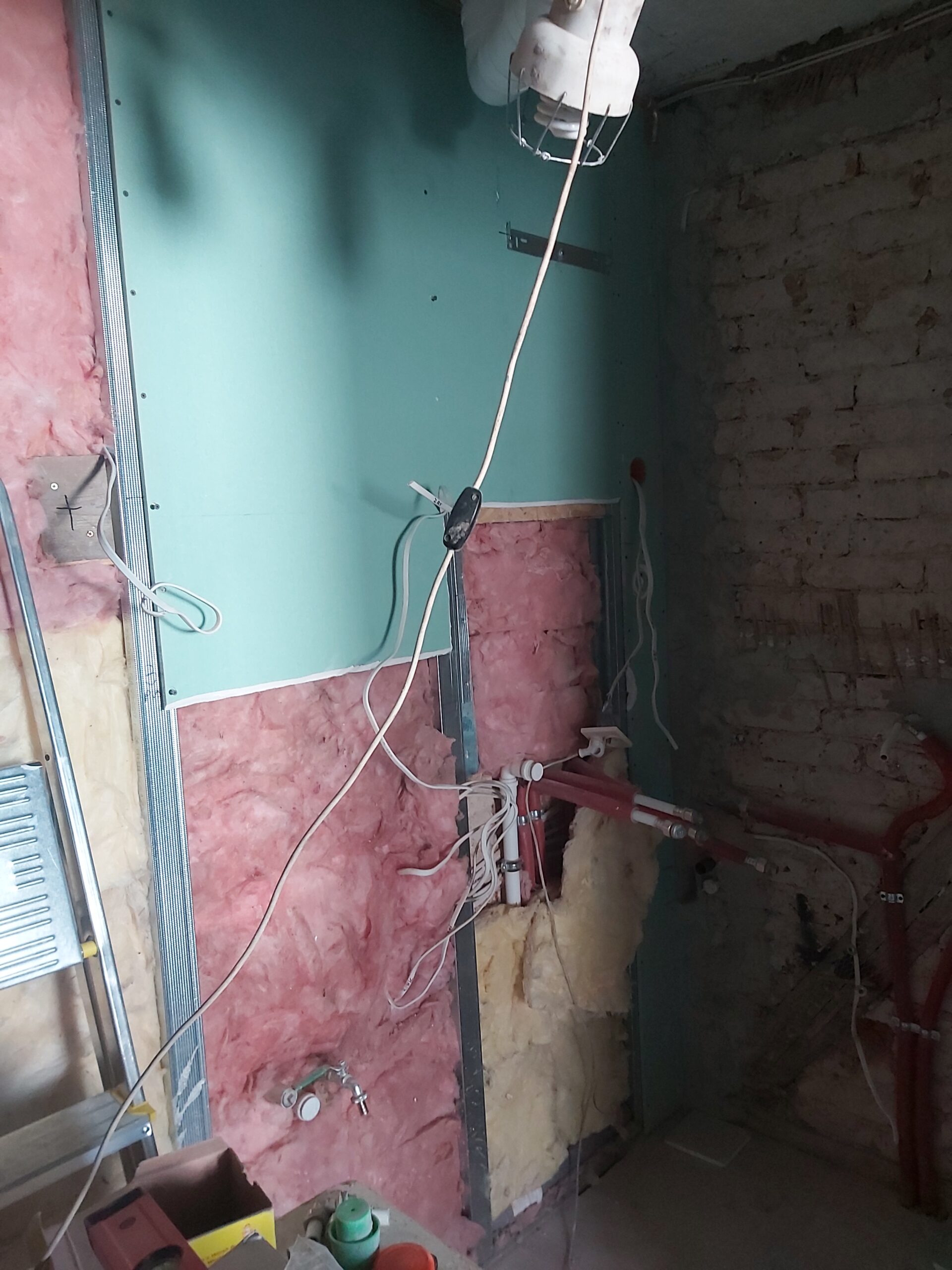 Odsłonięta instalacja wodno-kanalizacyjna i elektryczna w trakcie remontu pomieszczenia, z widoczną wełną mineralną, przewodami, rurami oraz konstrukcją pod płyty gipsowo-kartonowe.