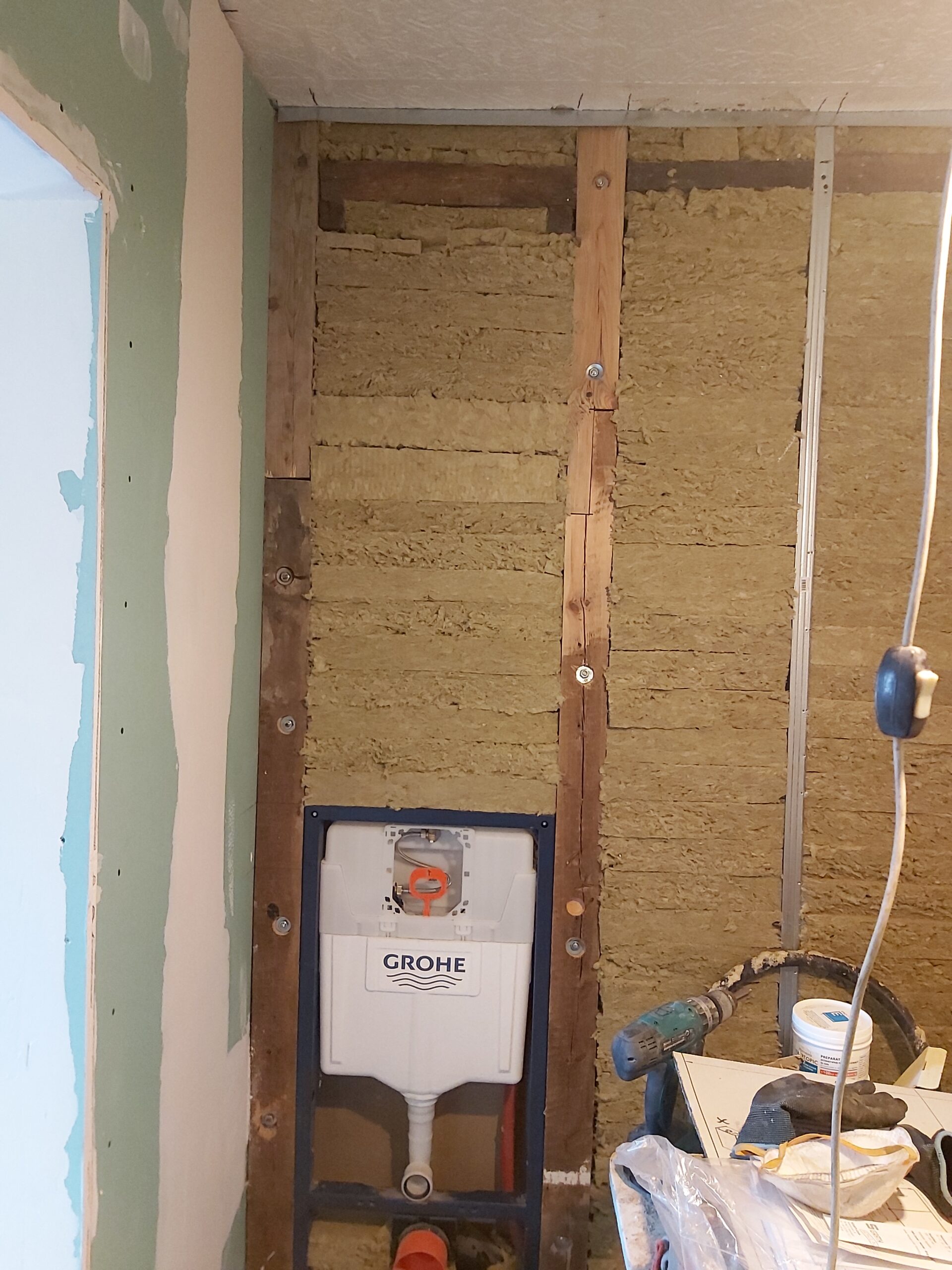Stelaż podtynkowy WC Grohe przed zabudową, z widoczną izolacją z wełny mineralnej i konstrukcją drewnianą w trakcie remontu łazienki.