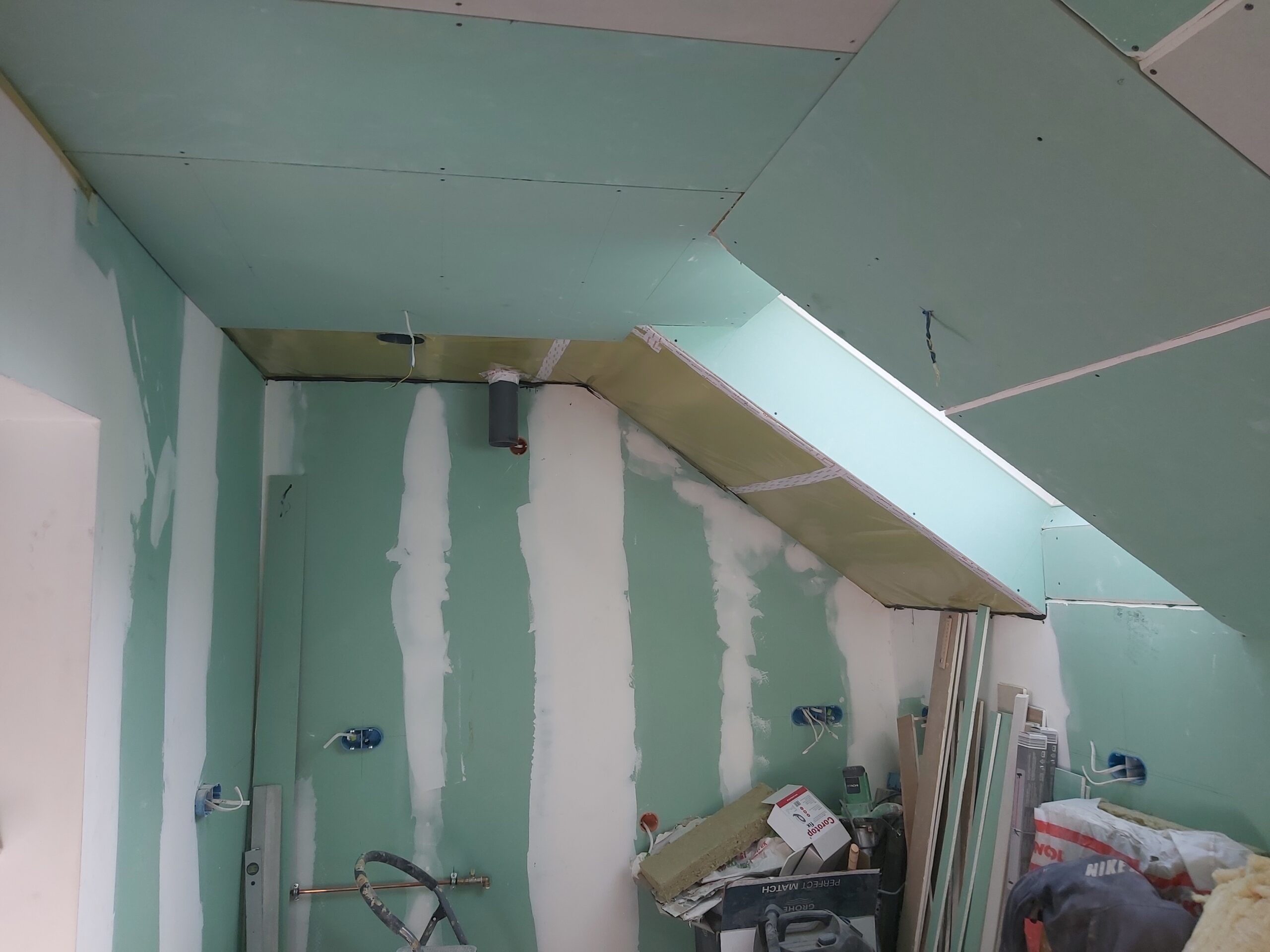 Zabudowa skosu poddasza z płyt gipsowo-kartonowych, ściana z instalacjami w trakcie szpachlowania