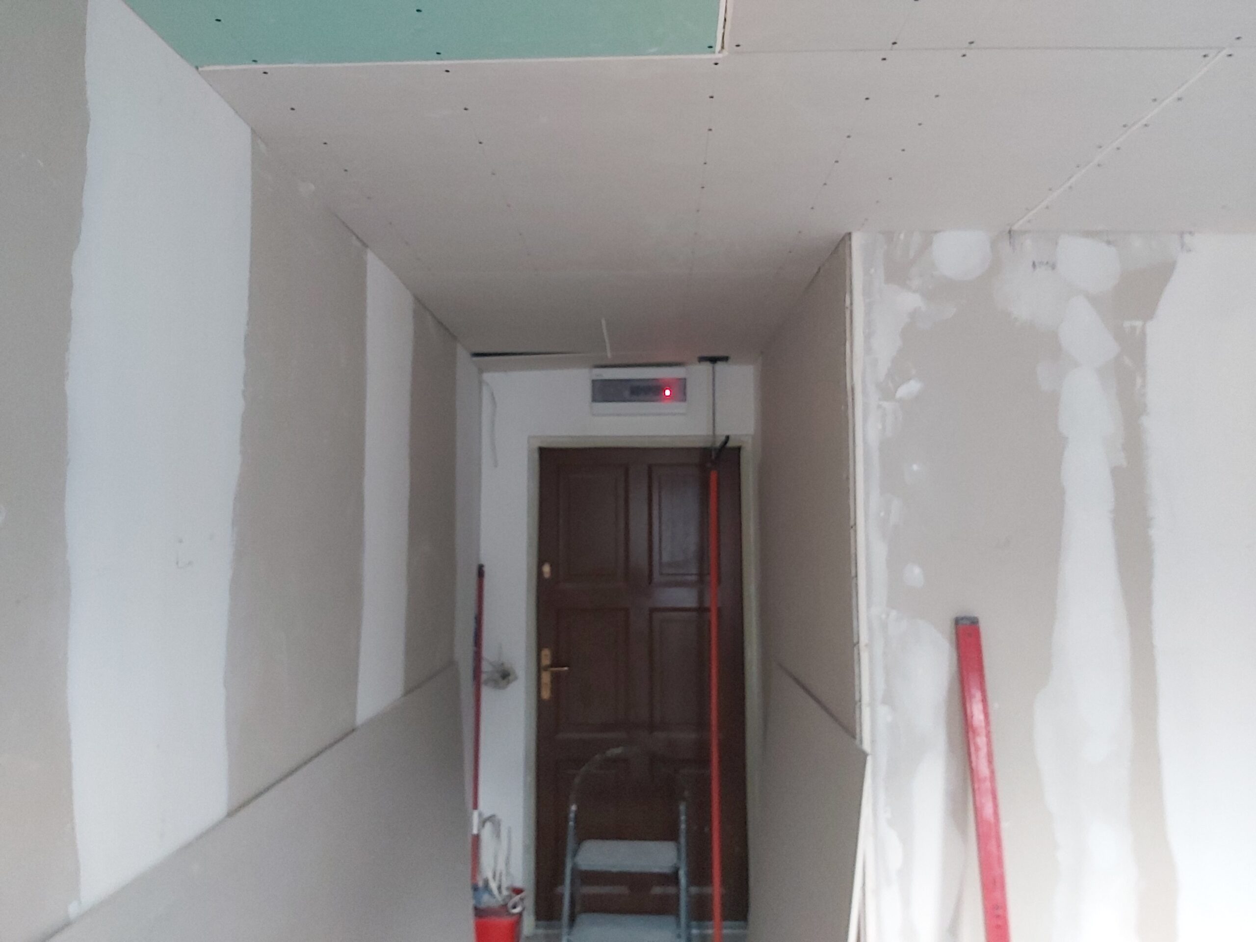 Korytarz w trakcie remontu z zabudową gipsowo-kartonową, szpachlowanymi ścianami i widocznymi narzędziami