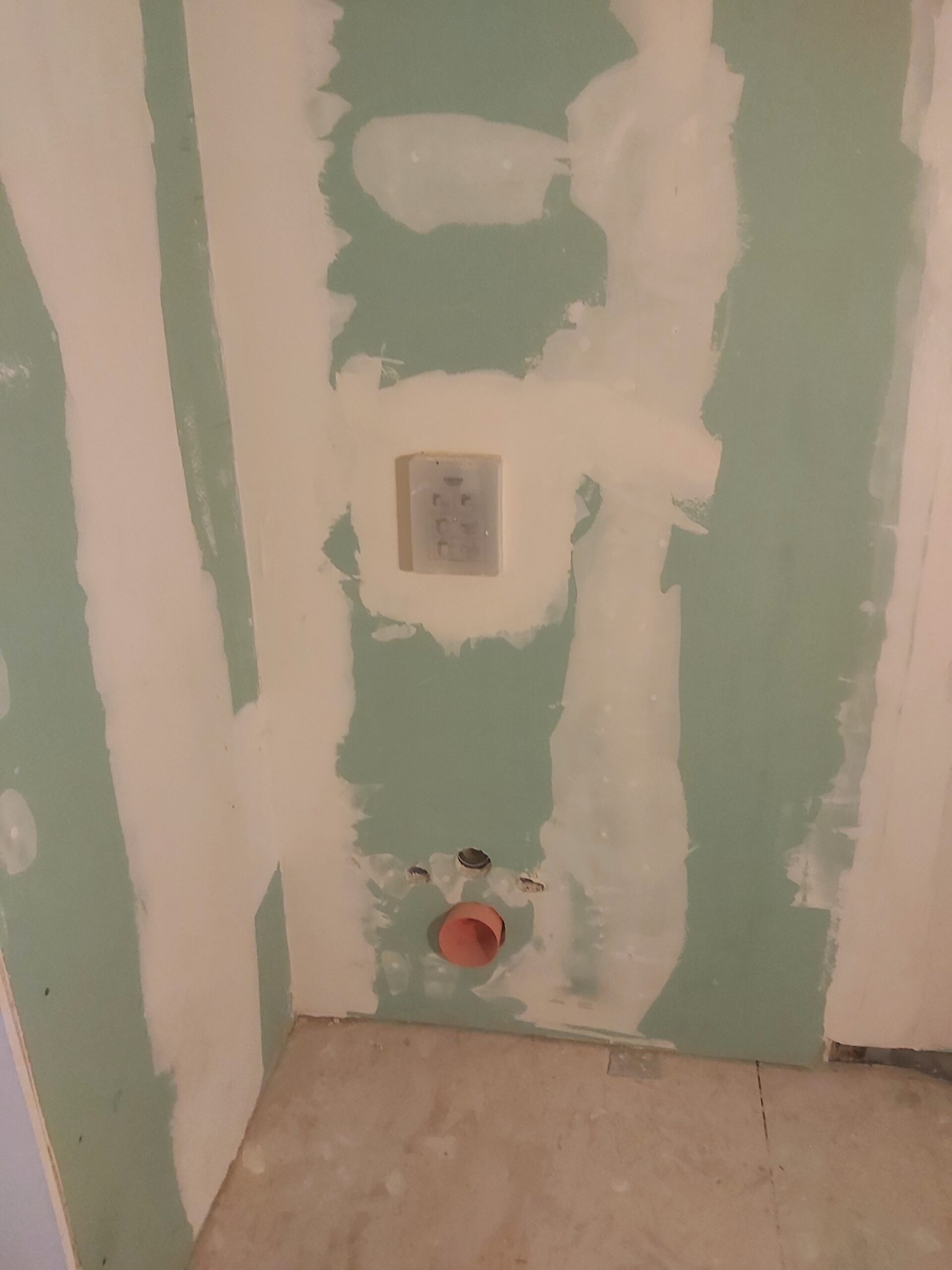 Przygotowane przyłącza instalacyjne w ścianie łazienki przed montażem ceramiki, widoczne wyprowadzenia oraz gniazdo elektryczne w trakcie remontu.