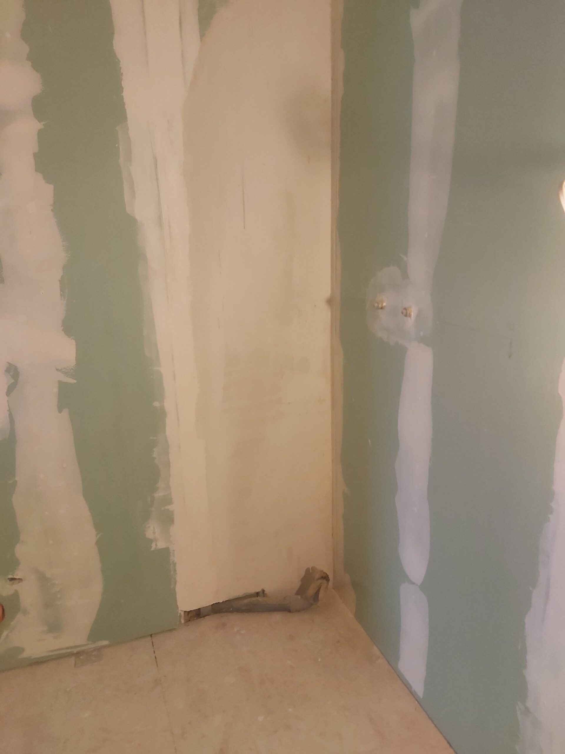 Narożnik ściany z płyt gipsowo-kartonowych w trakcie szpachlowania, z widocznymi pasami masy na łączeniach płyt oraz przygotowaną powierzchnią przy podłodze przed dalszymi pracami wykończeniowymi.