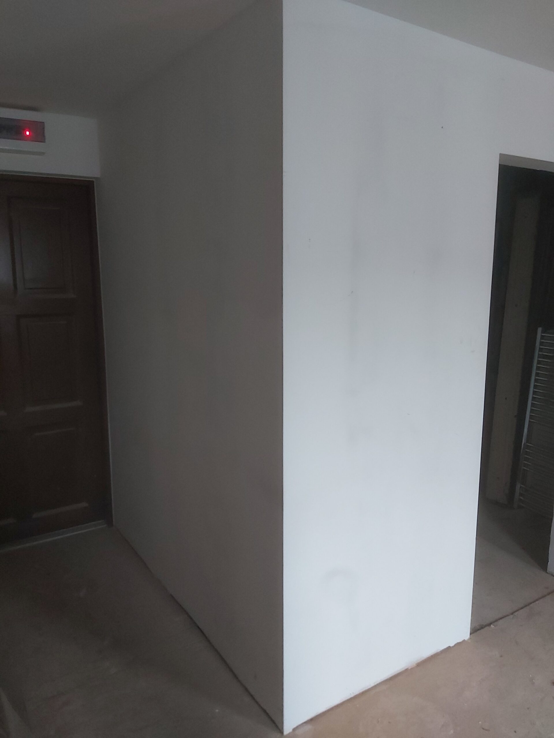 Narożnik nowo wykonanej ściany działowej z płyt kartonowo-gipsowych, widok na połączenie ściany z korytarzem podczas prac wykończeniowych.