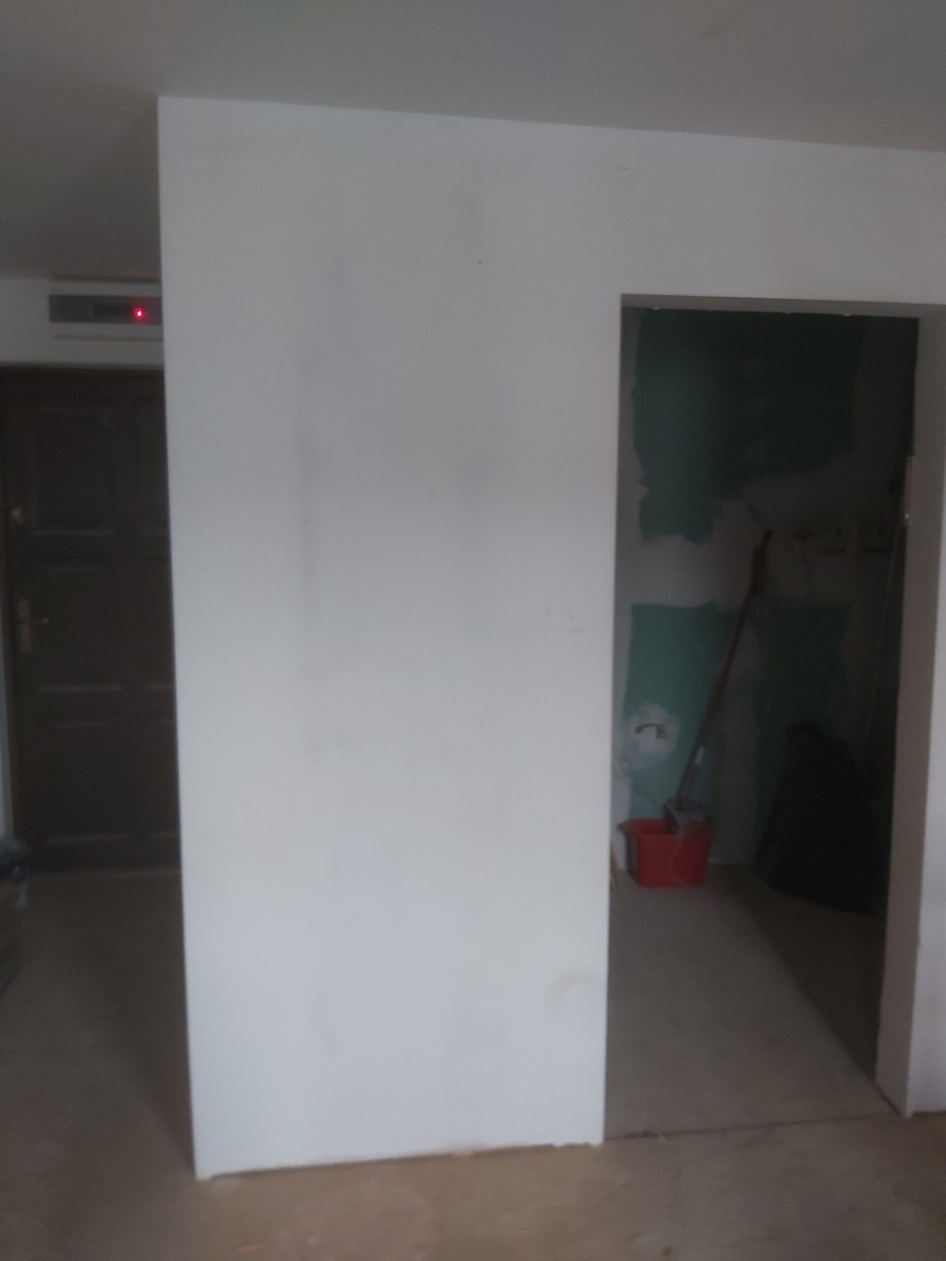 Nowa ściana działowa z płyt kartonowo-gipsowych z wykonanym otworem drzwiowym, widok podczas prac wykończeniowych w trakcie remontu wnętrza.