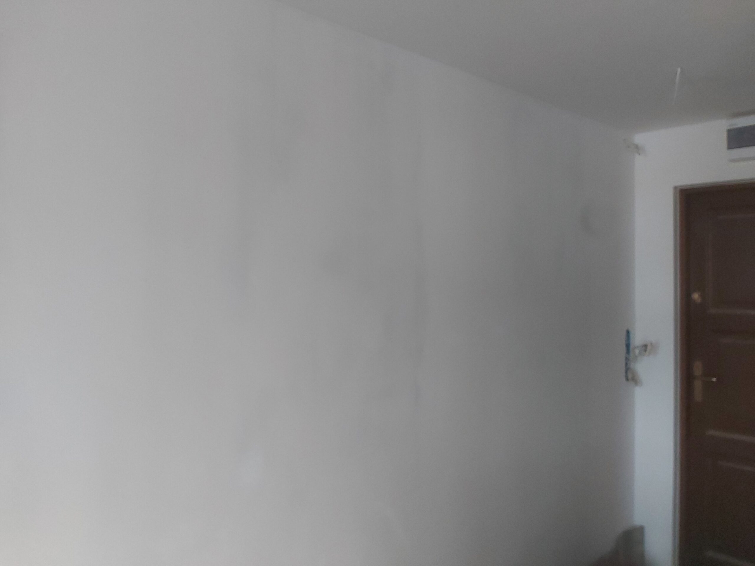 Biała ściana w korytarzu po szpachlowaniu i pierwszym malowaniu, z widocznymi smugami i różnicami w strukturze powierzchni przed dalszymi pracami wykończeniowymi.