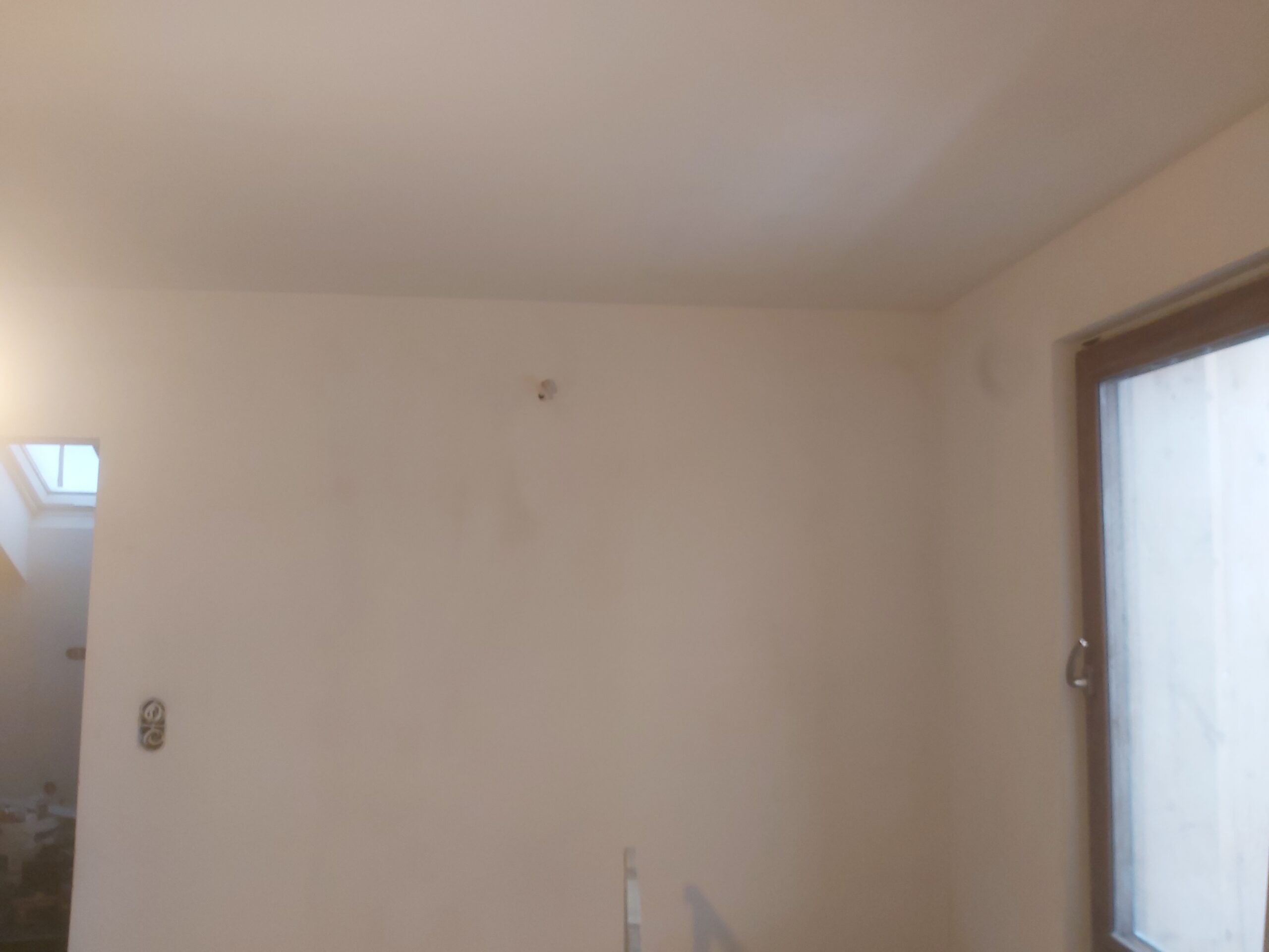 Jasna ściana wewnętrzna po zakończonym szpachlowaniu i malowaniu, przygotowana pod dalszą aranżację wnętrza, z widocznym oknem po prawej stronie.