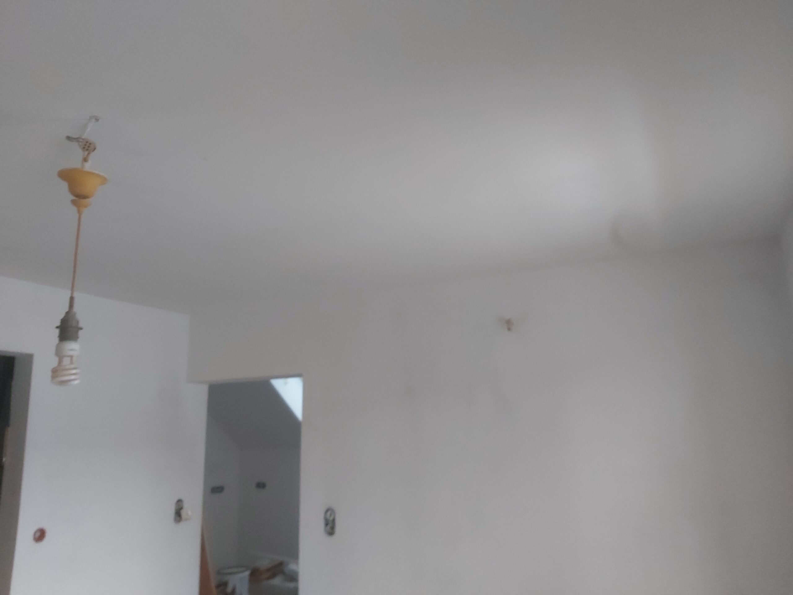 Ściana wewnętrzna po wstępnym szpachlowaniu, z widocznymi wyprowadzeniami instalacji wodnej i elektrycznej, przygotowana pod dalsze prace wykończeniowe.