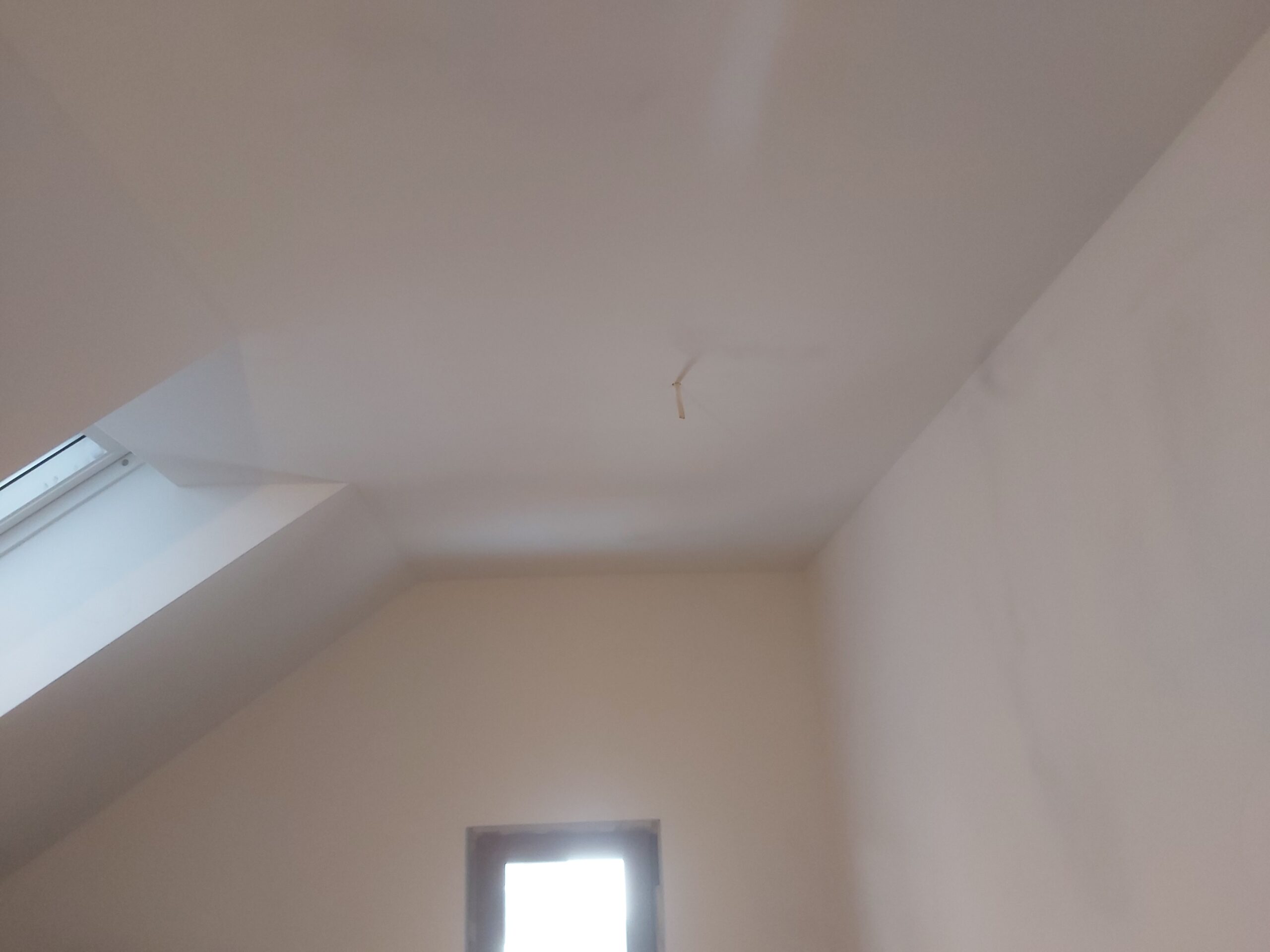 Wykończony sufit i ściany na poddaszu z oknem pionowym, widoczne miejsce pod oświetlenie