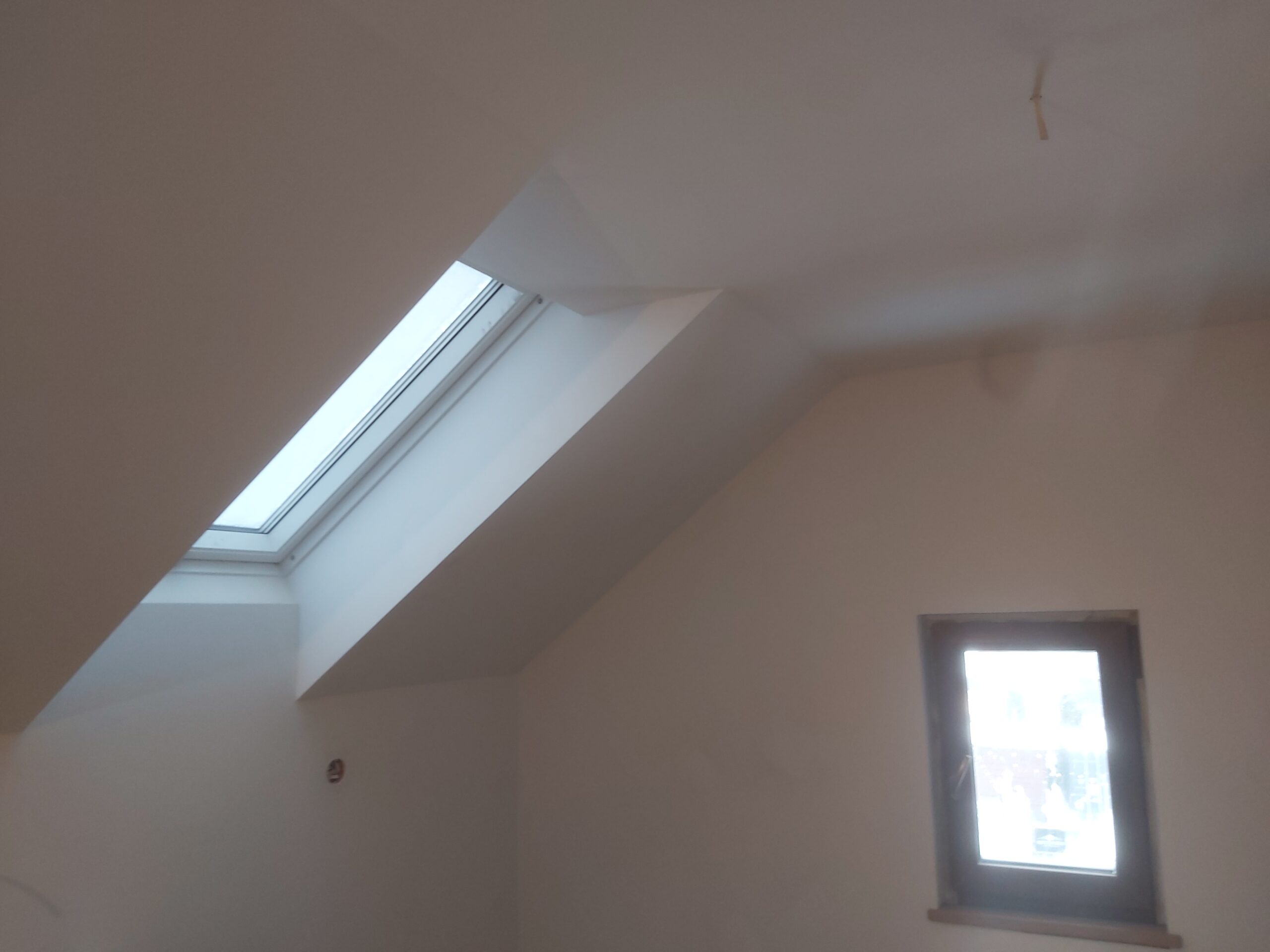 Skośny sufit z oknem dachowym i pionowym oknem, wnętrze po pracach wykończeniowych