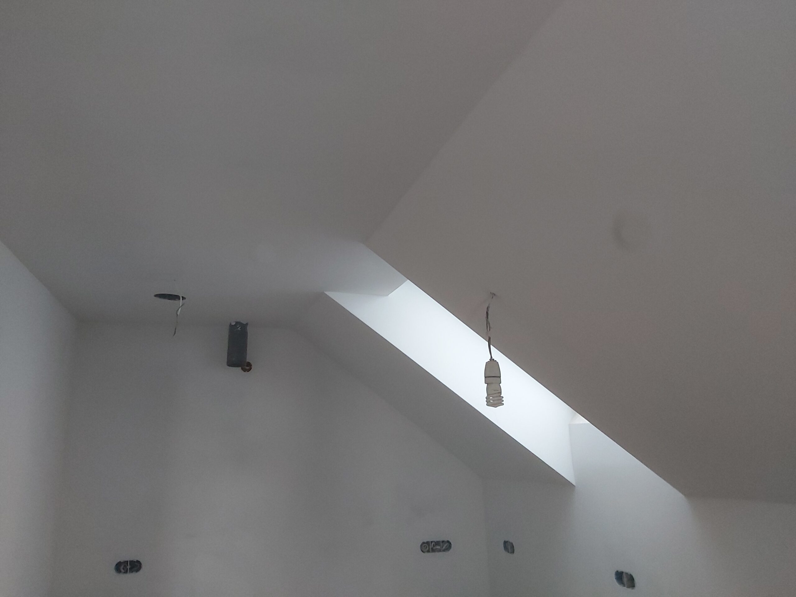 Biały sufit ze skosem i oknem dachowym, instalacja oświetleniowa przygotowana do montażu