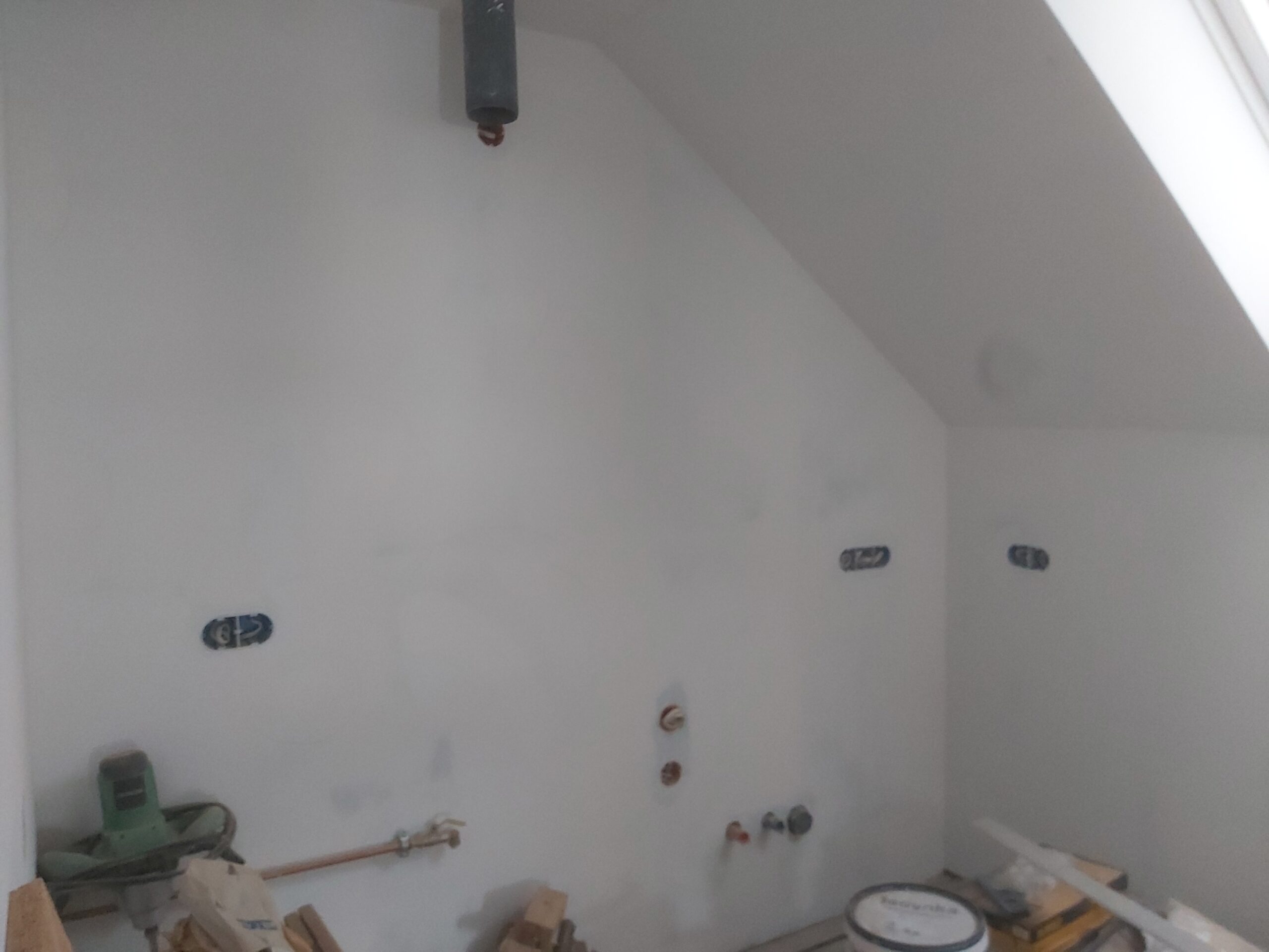 Ściana wewnętrzna po wstępnym szpachlowaniu, z widocznymi wyprowadzeniami instalacji wodnej i elektrycznej, przygotowana pod dalsze prace wykończeniowe.