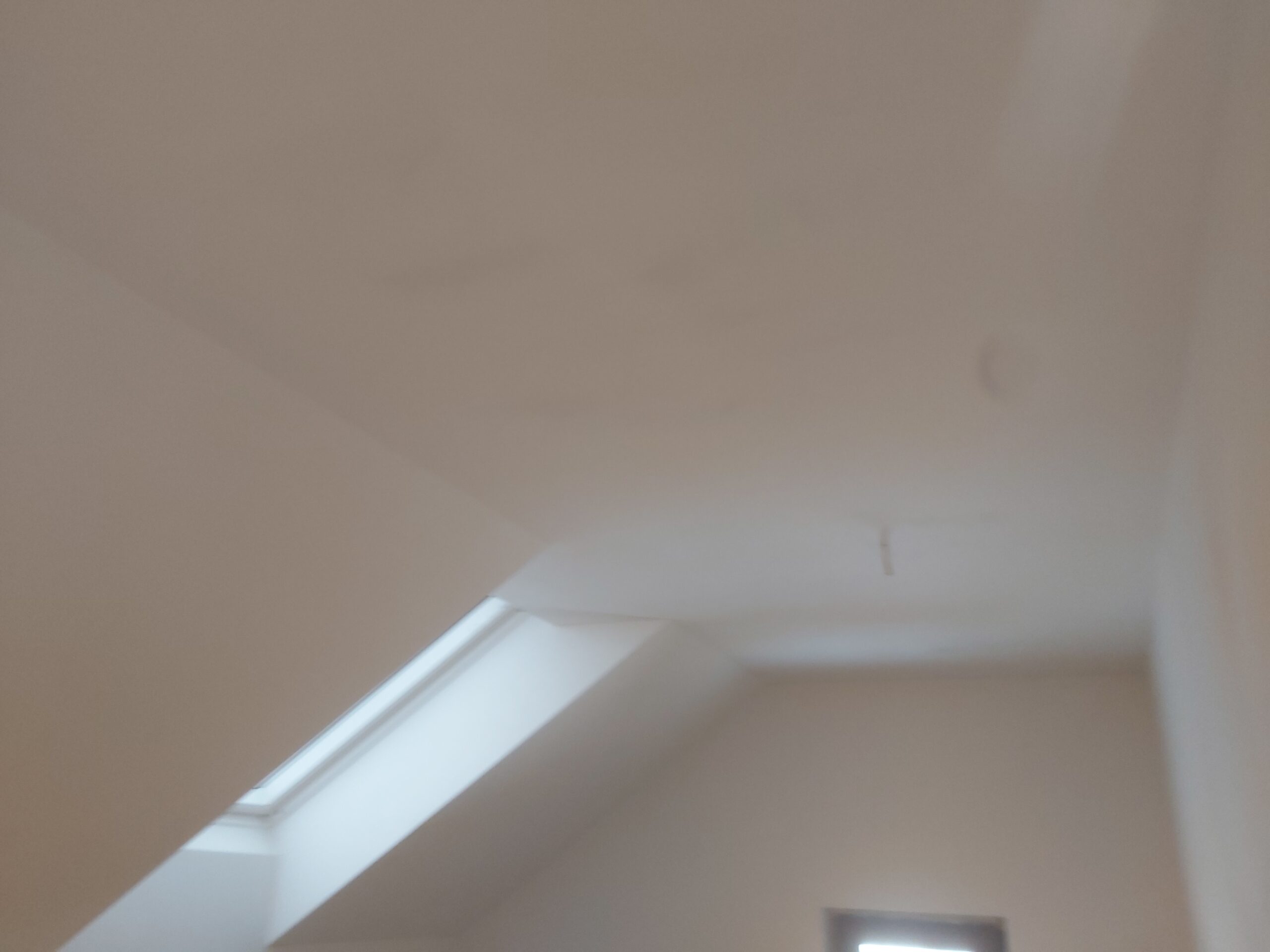 Wykończony biały sufit ze skosem i oknem dachowym po pracach remontowych