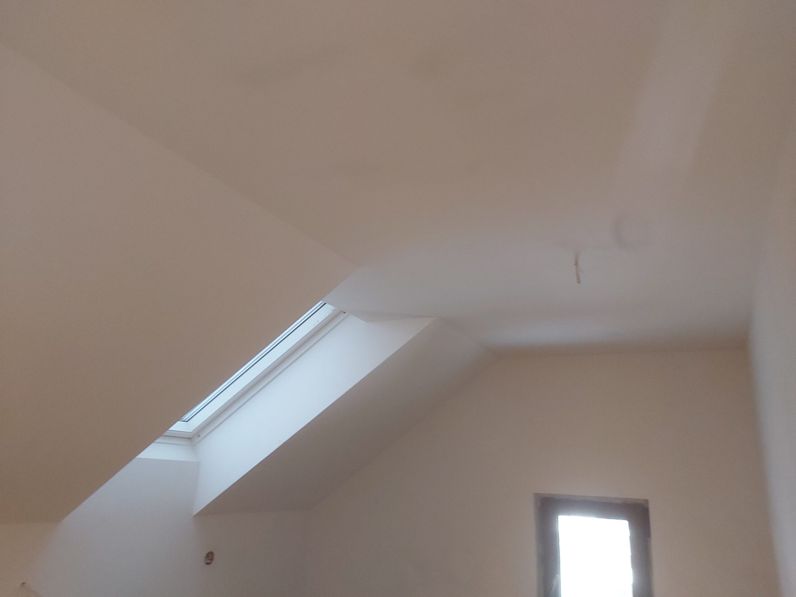 Wykończony sufit i skos z oknem dachowym po remoncie, białe ściany, gotowa powierzchnia do malowania