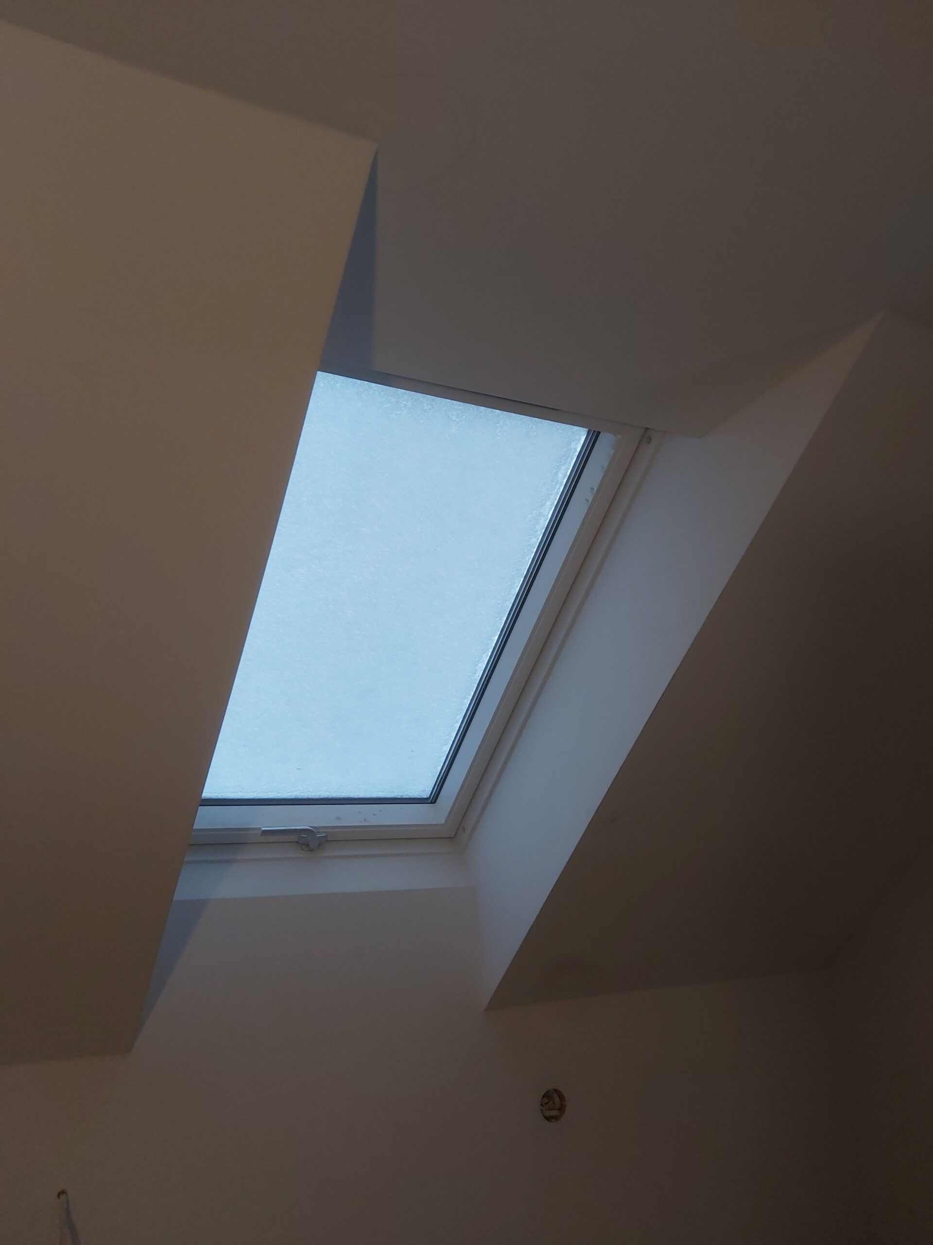 Okno dachowe po wykończeniu, osadzone między gładkimi skosami sufitu