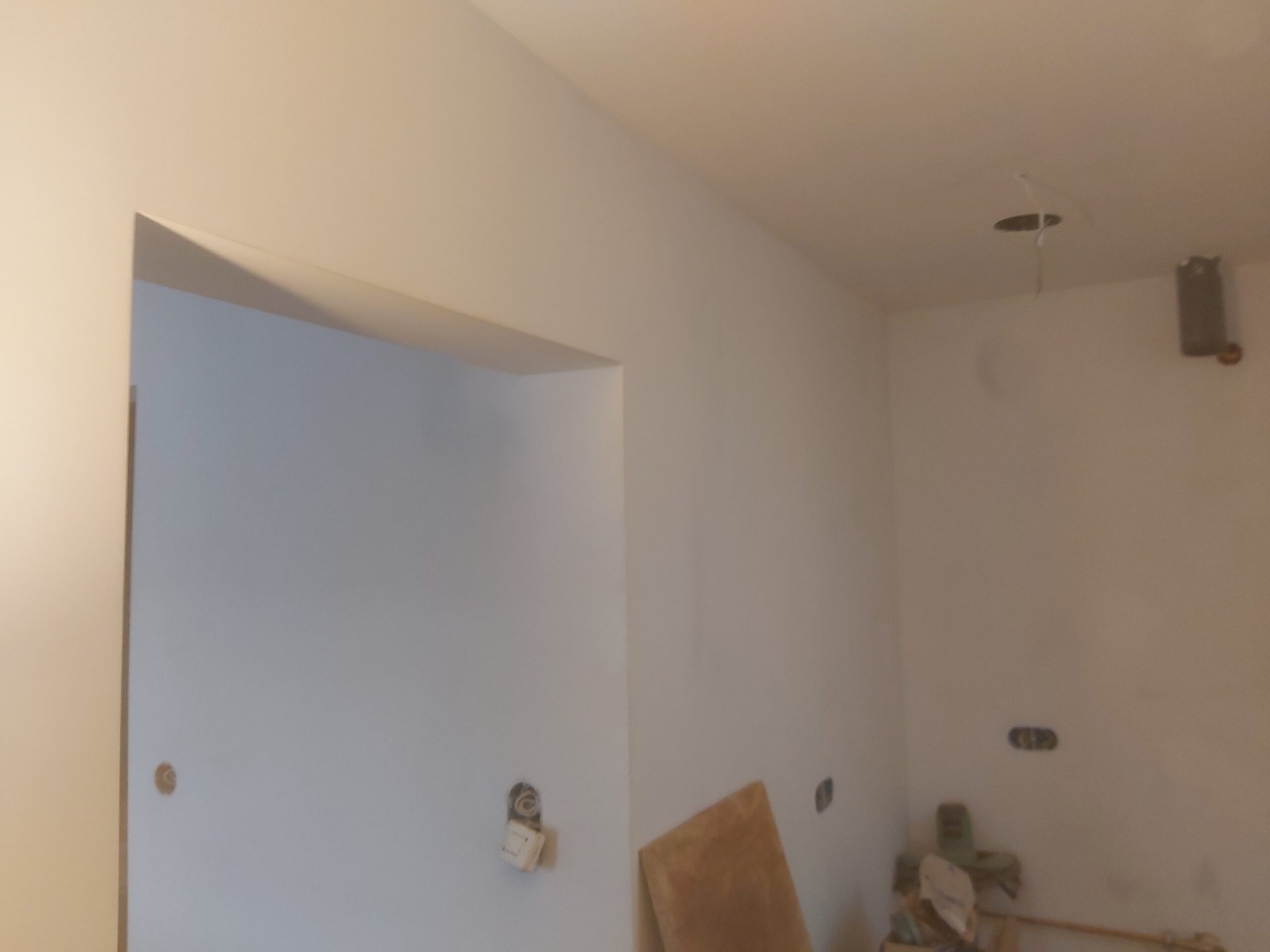 Wnętrze pomieszczenia po wstępnym szpachlowaniu ścian i sufitu, z widocznym otworem drzwiowym oraz przygotowanymi punktami instalacyjnymi.