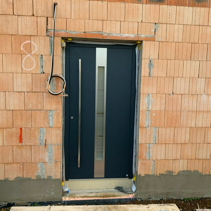 Nowoczesne drzwi zewnętrzne w kolorze antracytowym zamontowane w murze z pustaków ceramicznych podczas budowy domu.