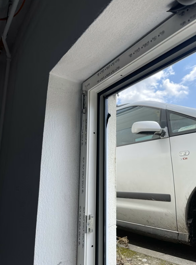 Zbliżenie na narożnik białego okna piwnicznego z ramą PVC i wykończoną wnęką, widok od wewnątrz.