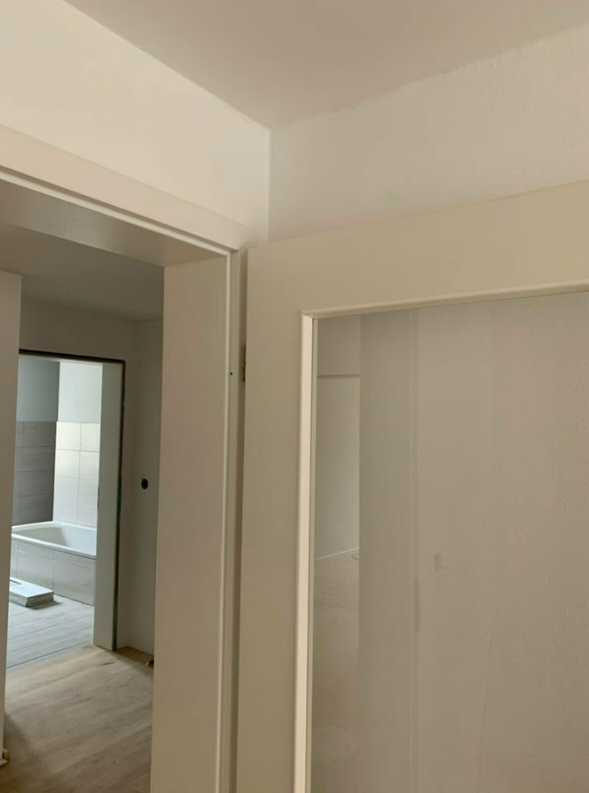 Wykończone ościeżnice drzwiowe w jasnym wnętrzu, pokazujące równe krawędzie ścian i spójne przejście między pomieszczeniami po remoncie.