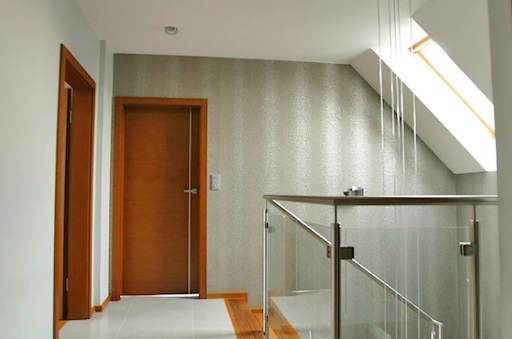Nowoczesny korytarz z drewnianymi drzwiami, szklaną balustradą i ścianą o dekoracyjnej fakturze.
