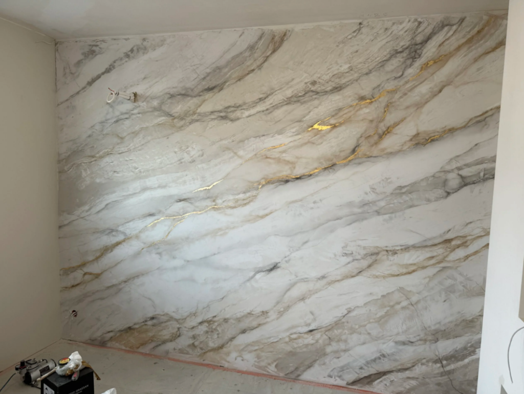 Dekoracyjna ściana ze stiuku weneckiego z efektem marmuru w jasnych odcieniach z złotymi żyłami.