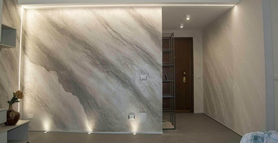Ściana w przedpokoju wykończona stiukiem weneckim z efektem marmuru w jasnych odcieniach, podświetlona oświetleniem LED.