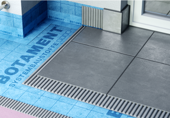 Zbliżenie na strefę prysznica typu walk-in z odpływem liniowym, płytkami podłogowymi oraz niebieską warstwą hydroizolacji zabezpieczającą podłoże i połączenia przy ścianie.