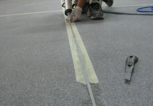 Pracownik aplikuje masę uszczelniającą w szczelinę dylatacyjną w posadzce, przygotowując trwałe i elastyczne wykończenie podłogi.