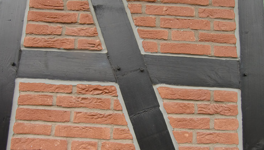 Zbliżenie na fragment elewacji z cegły klinkierowej z widoczną szczeliną dylatacyjną i czarnymi elementami konstrukcyjnymi.