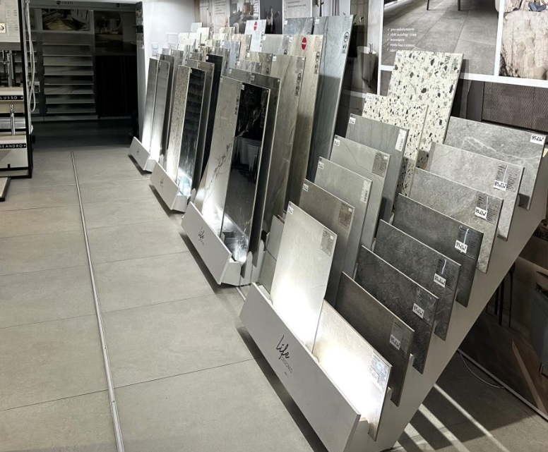 Salon sprzedaży z ekspozycją płytek ceramicznych i gresowych w różnych formatach, kolorach i wykończeniach, prezentowanych na stojakach wystawowych.