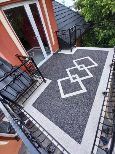 Balkon wykończony kamiennym dywanem w kolorze grafitowym z jasną ramką i geometrycznym wzorem dekoracyjnym na posadzce.